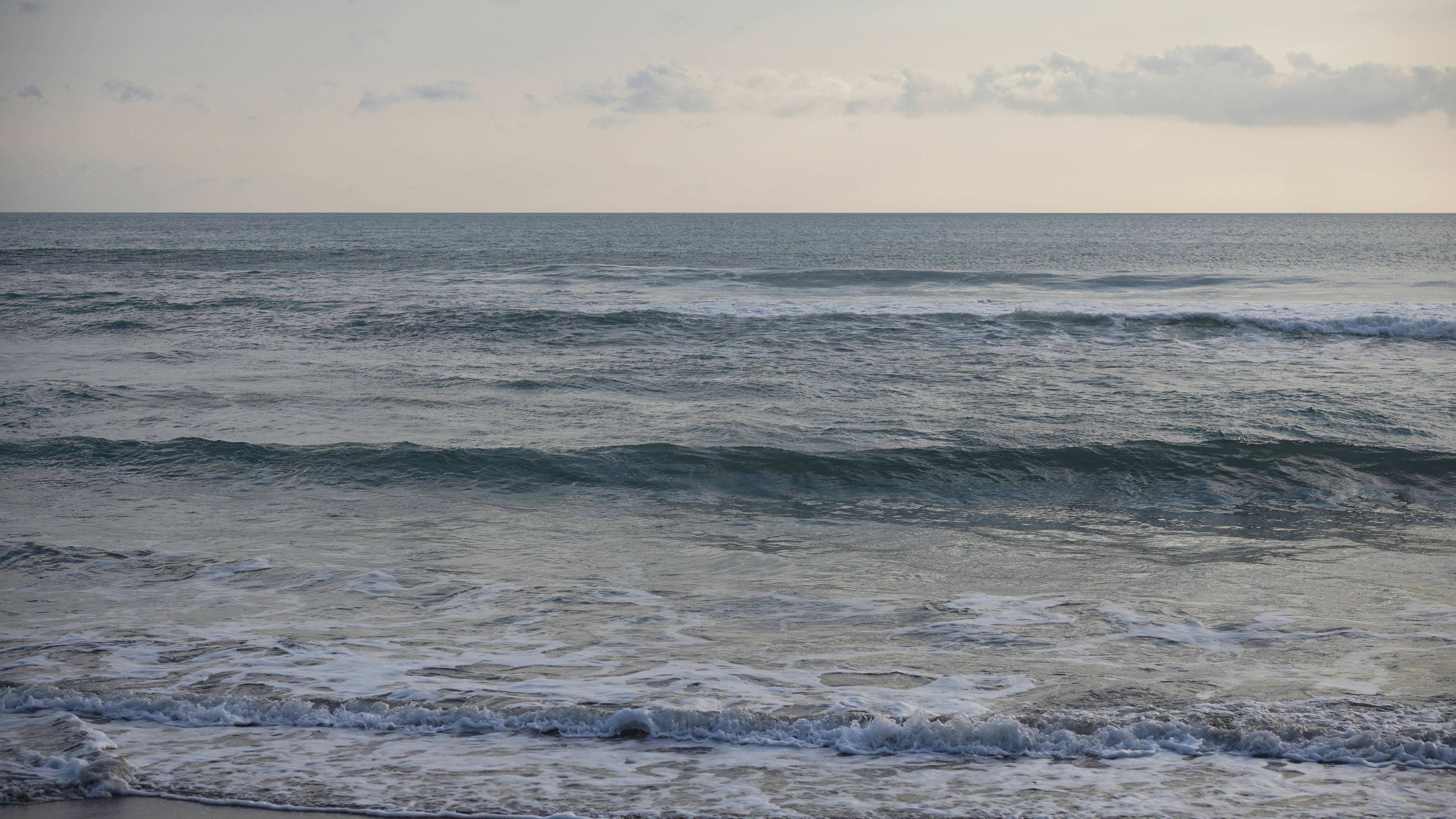 Gentle waves roll onto a sandy beach at dusk.