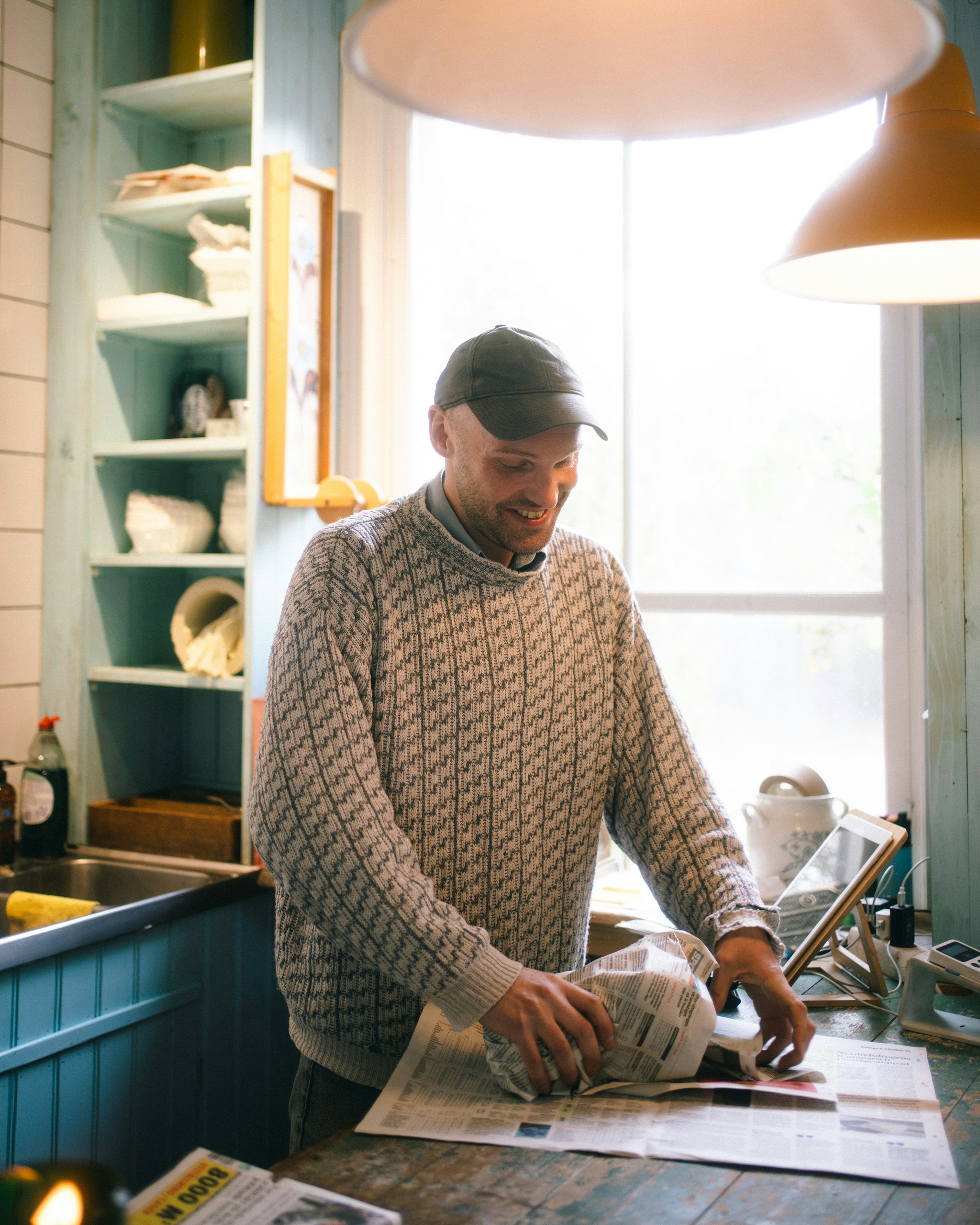 Man in a patterned sweater wrapping an object in newspaper.