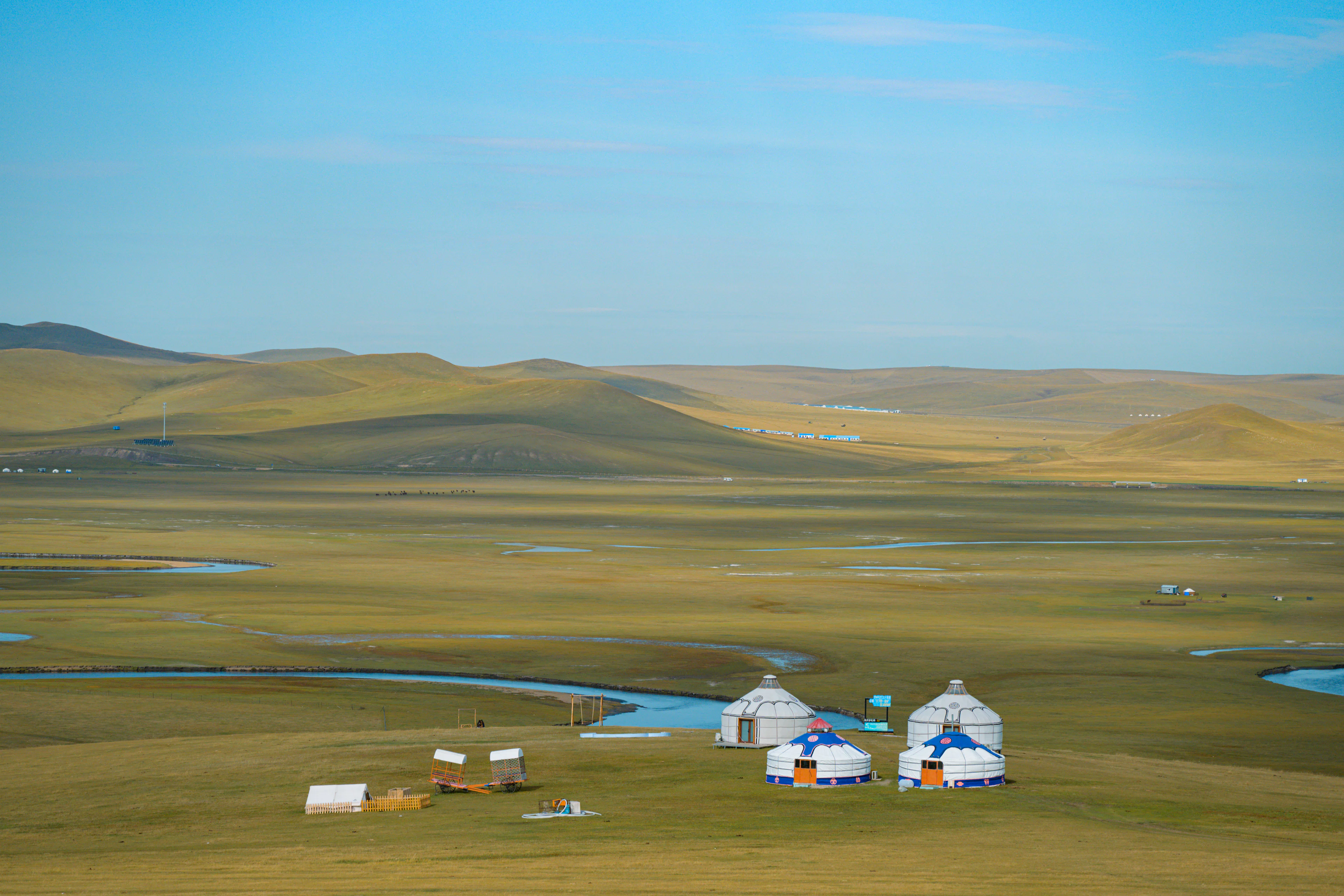 A cluster of gers beside a winding river on rolling green steppe