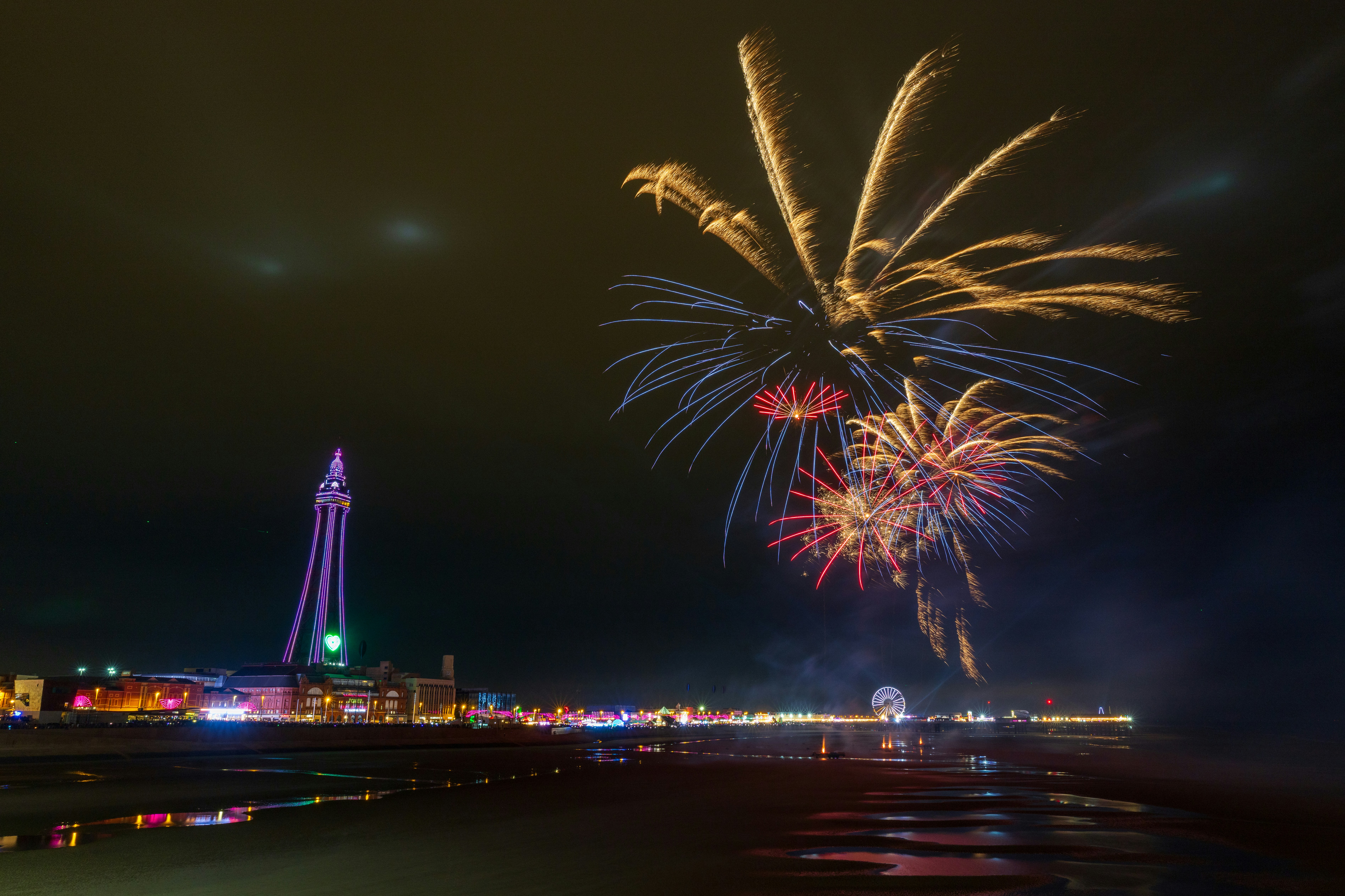 Fireworks explode over a coastal town at night.