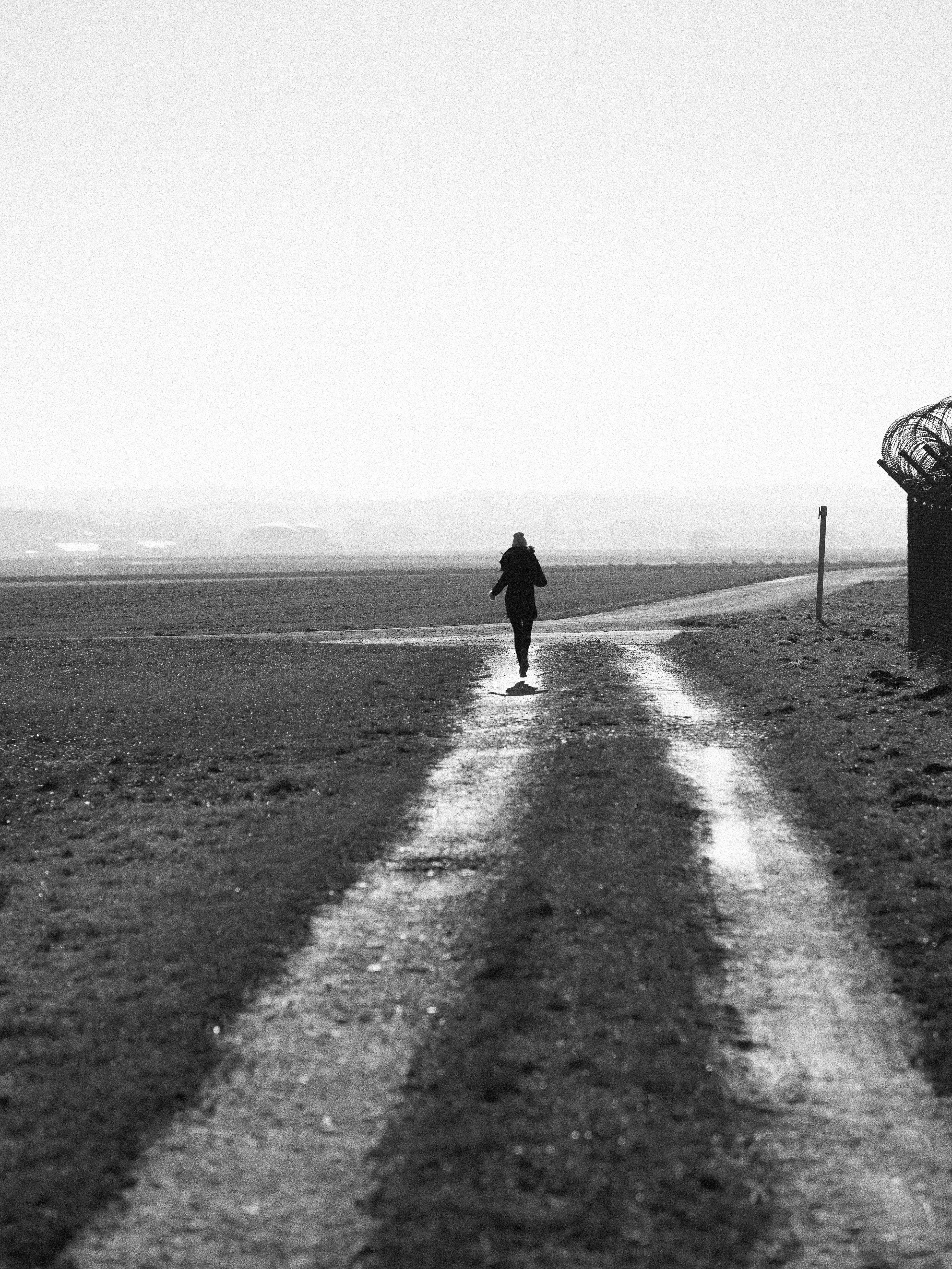 A person walks down a dirt road in a field.