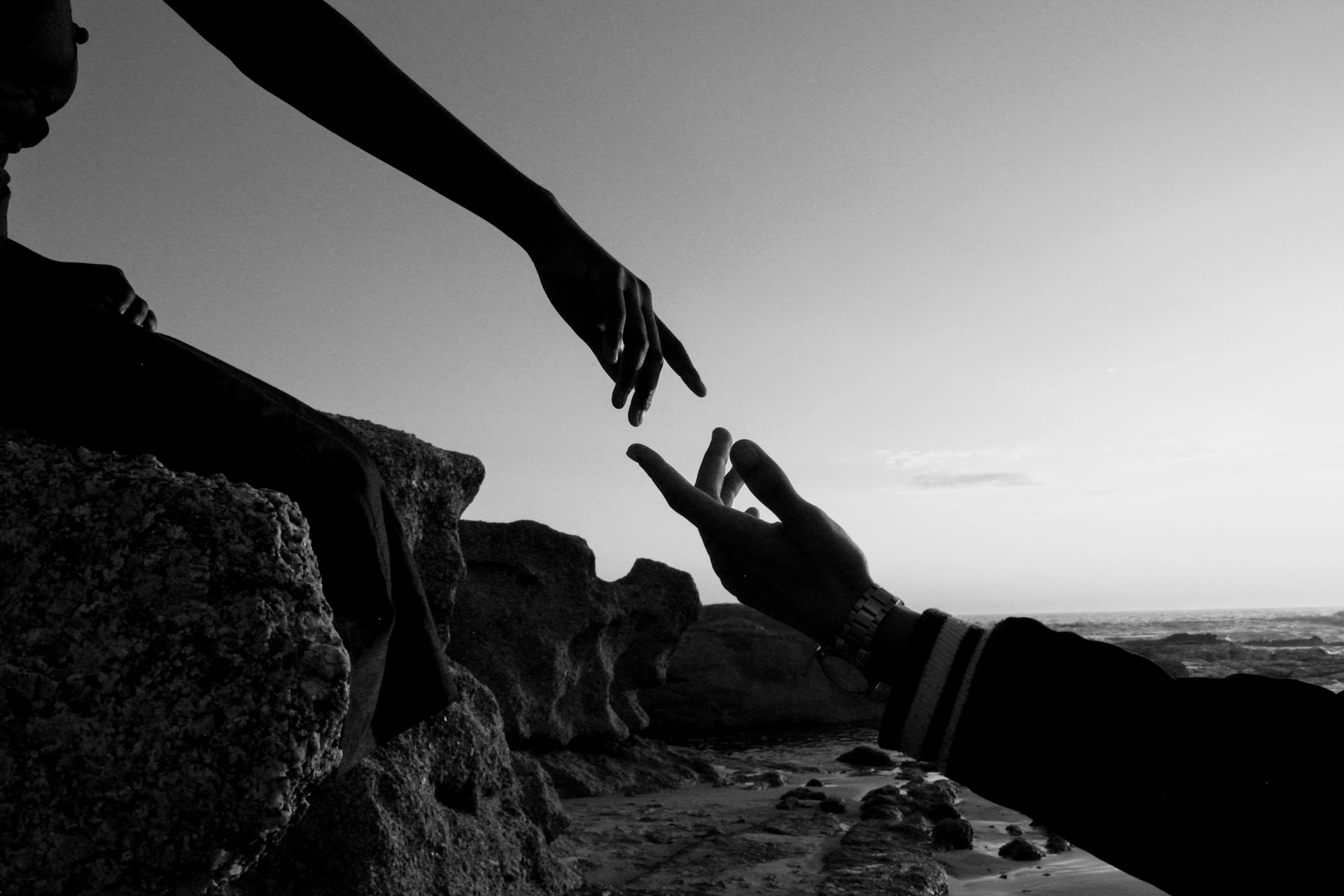 Two hands reaching towards each other at sunset