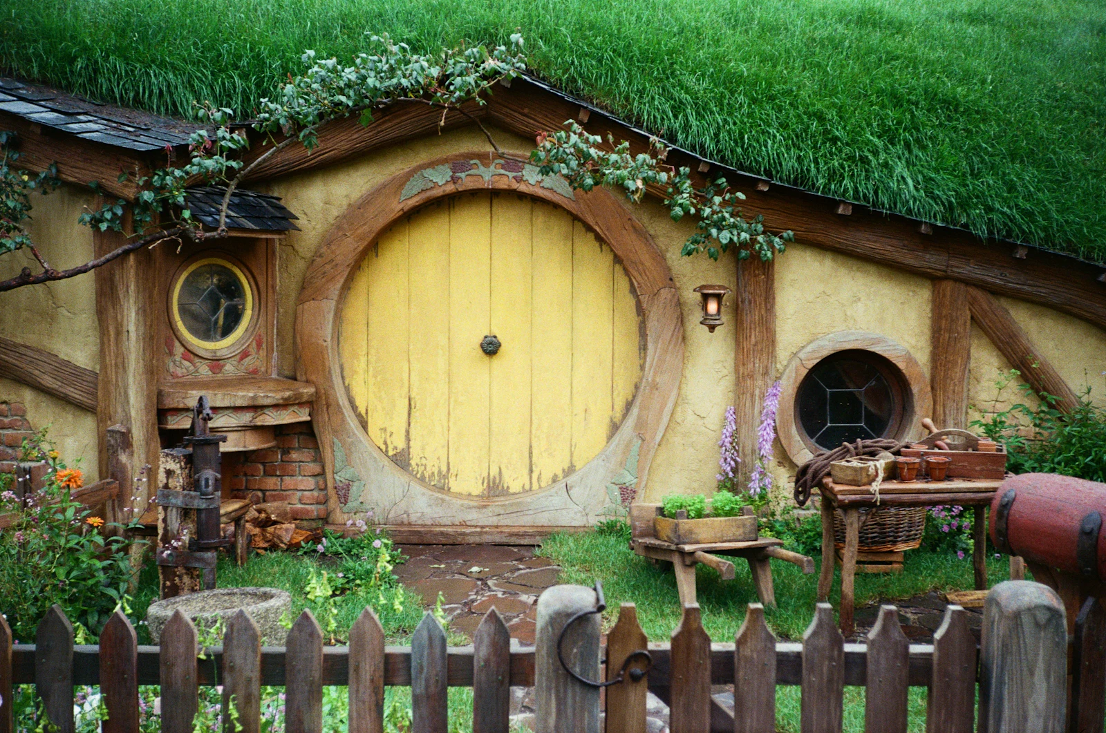 A round yellow door in a turf roofed bank, with a bench and a basket outside.
