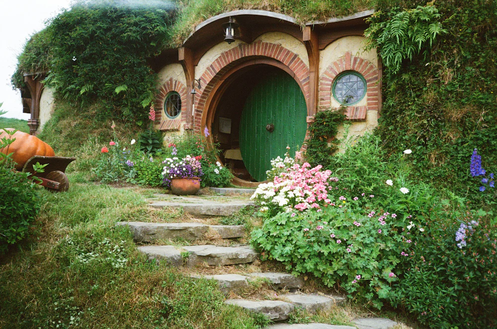 A round green door set into a grassy bank, stone steps and flowers in front.