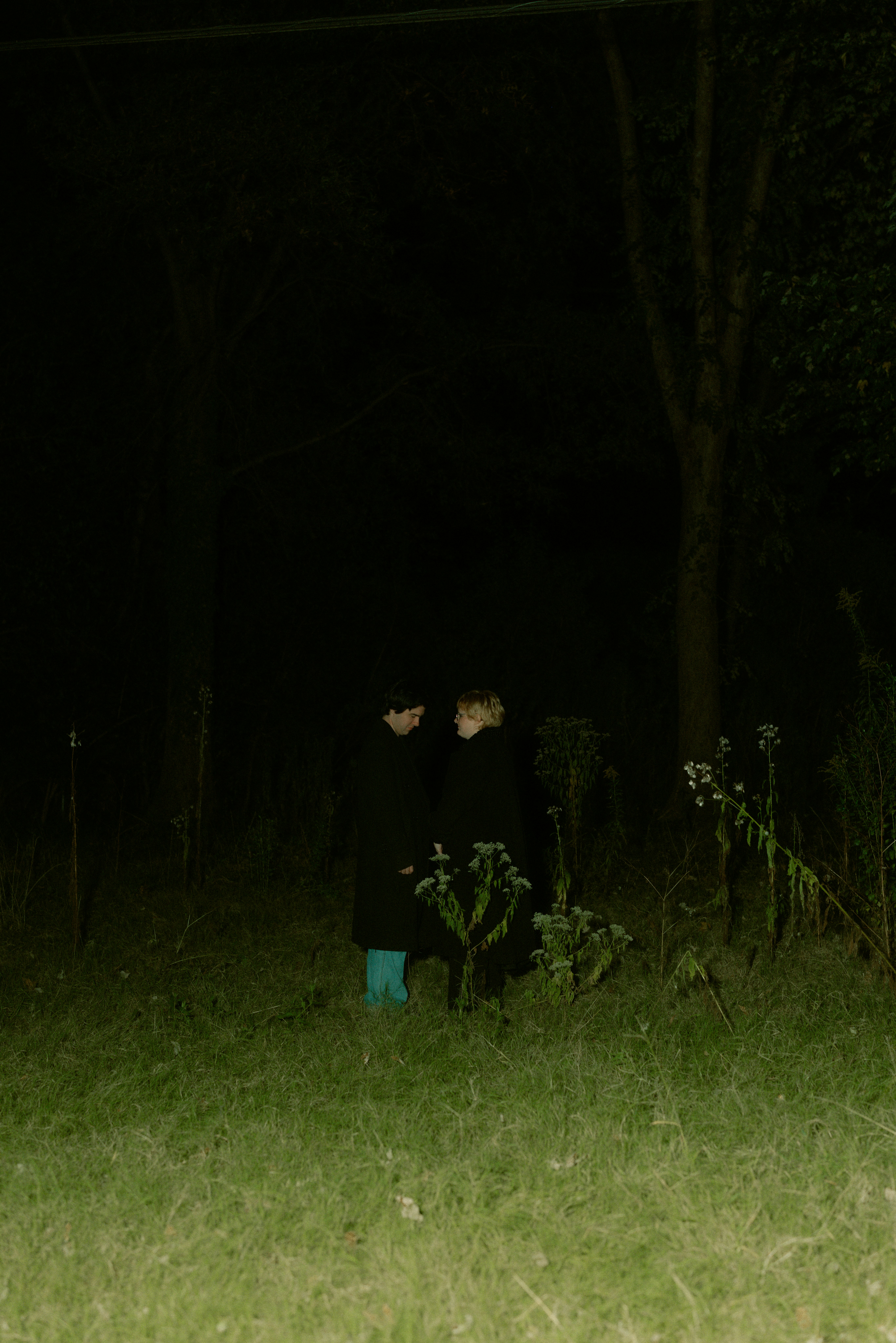 Duas pessoas estão em um campo escuro e gramado à noite.