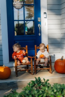 Two babies sitting in rocking chairs with pumpkins