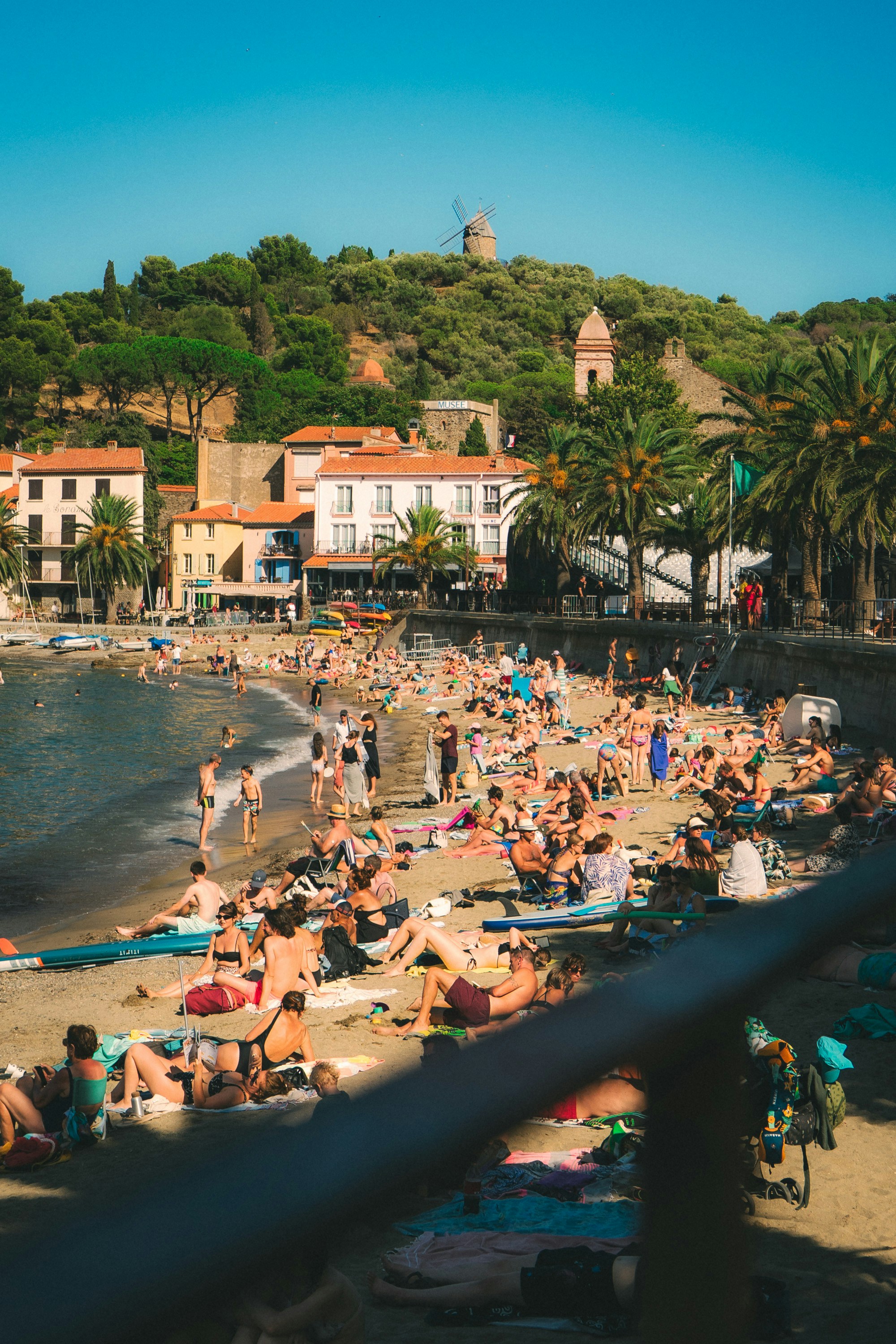 Crowded beach with people sunbathing and swimming in ocean.