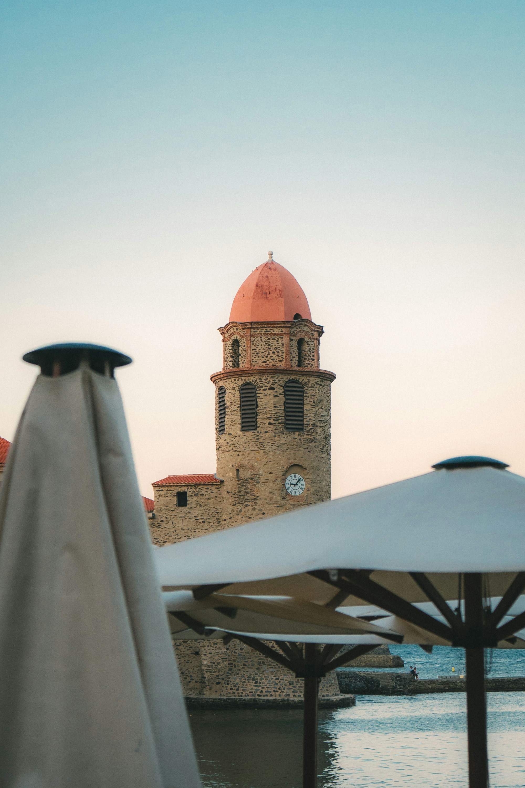 Stone tower with red dome near water and umbrellas