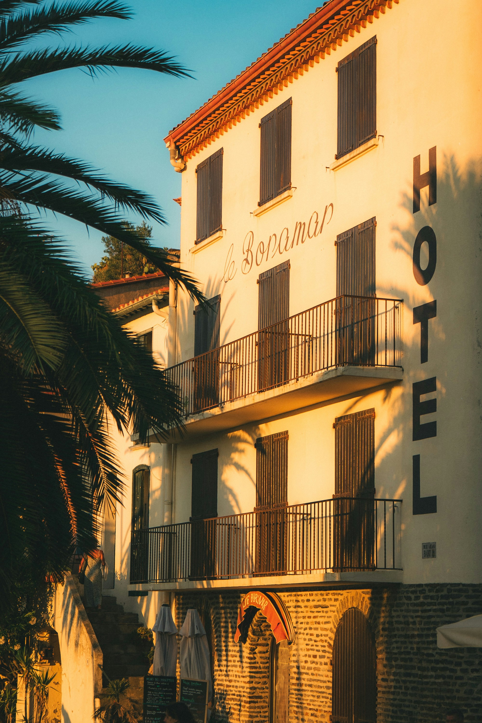 Hotel building with balconies and palm trees at sunset.
