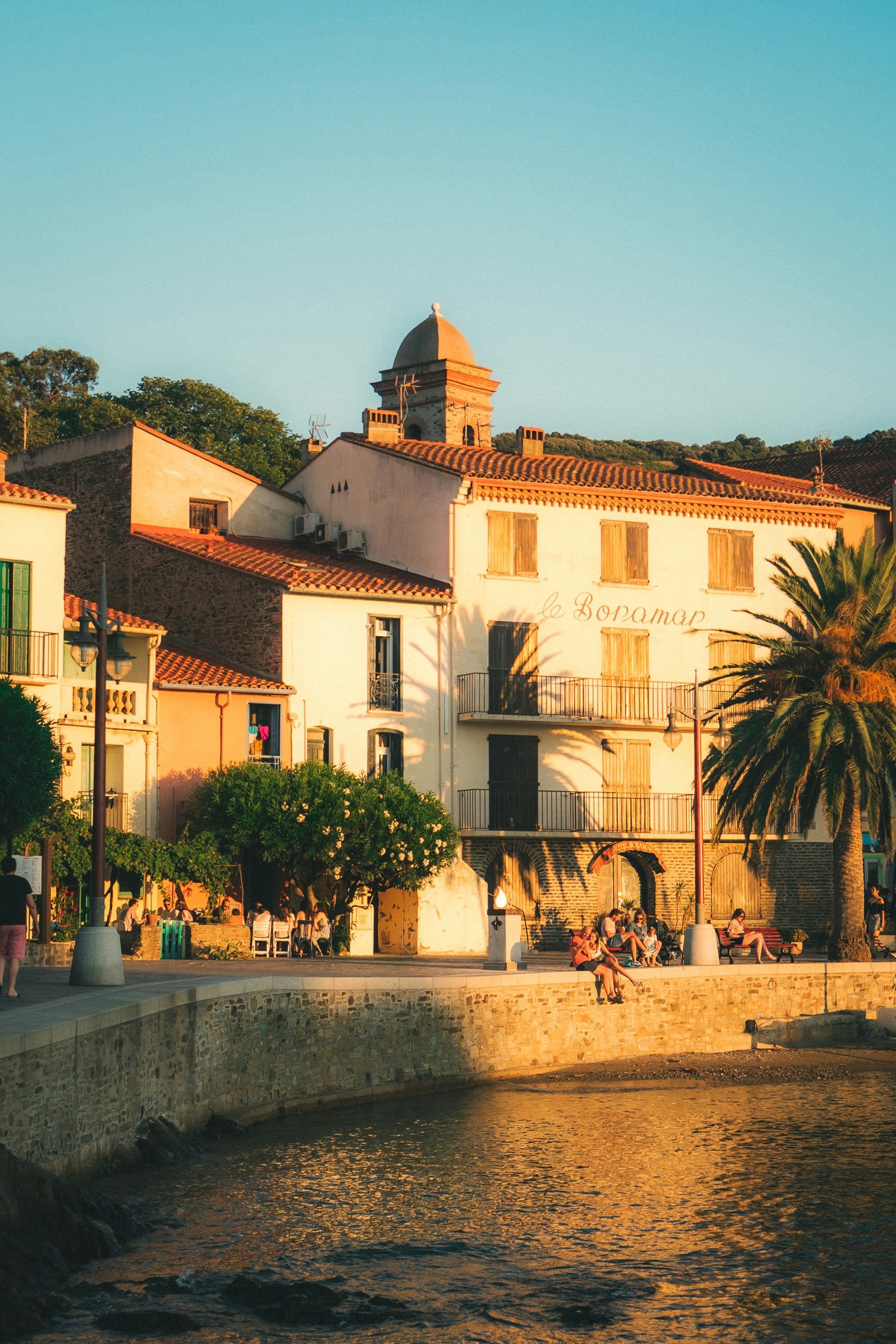 Coastal town buildings with people relaxing by the water.