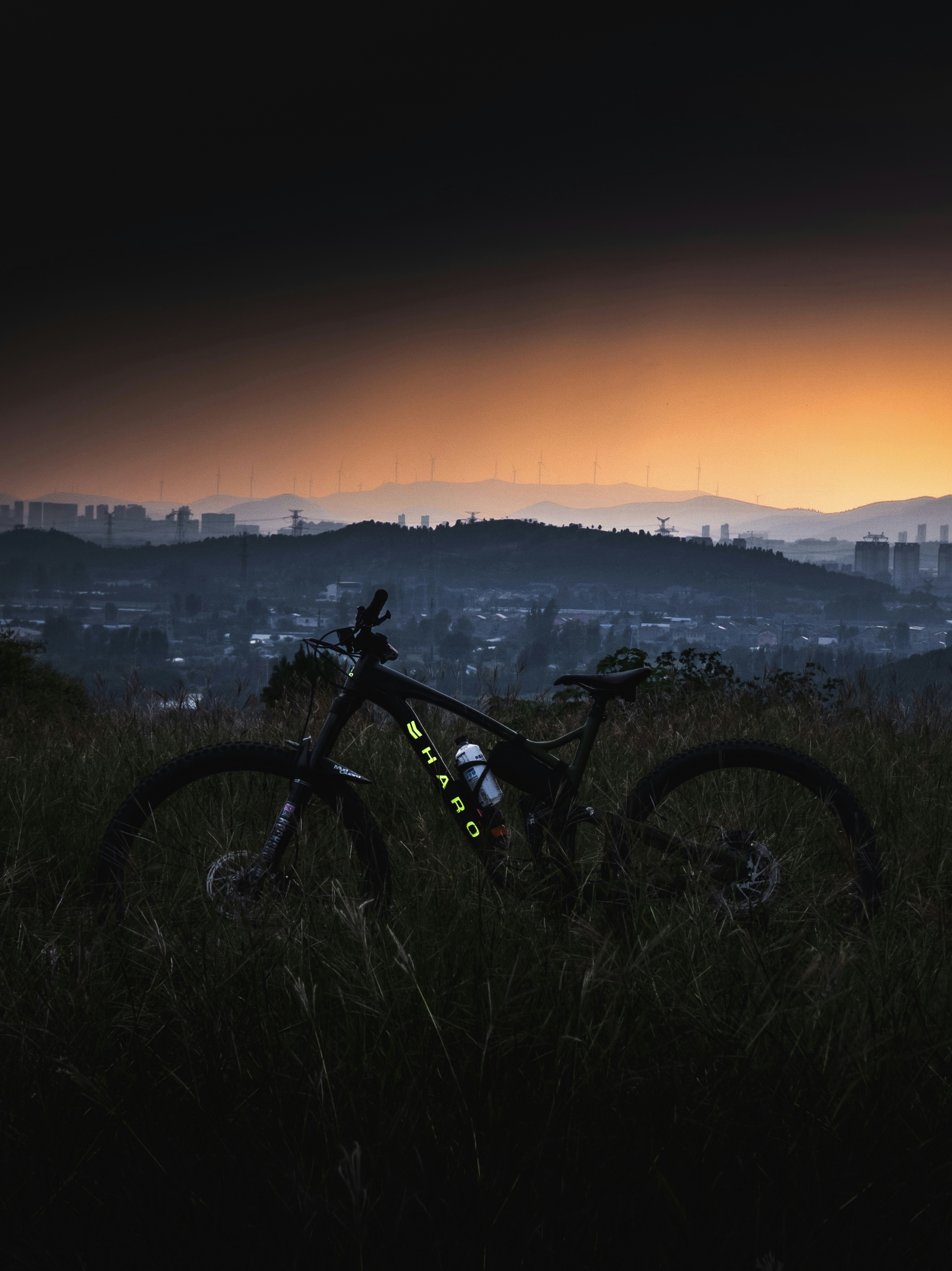 Mountain bike rests on grassy hill overlooking city at dusk
