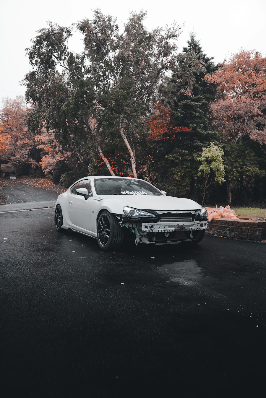 White car with a damaged front bumper parked on a wet road