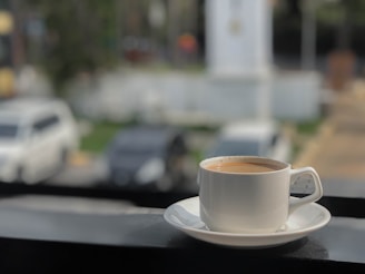 Cup of coffee on a saucer with cars blurred background