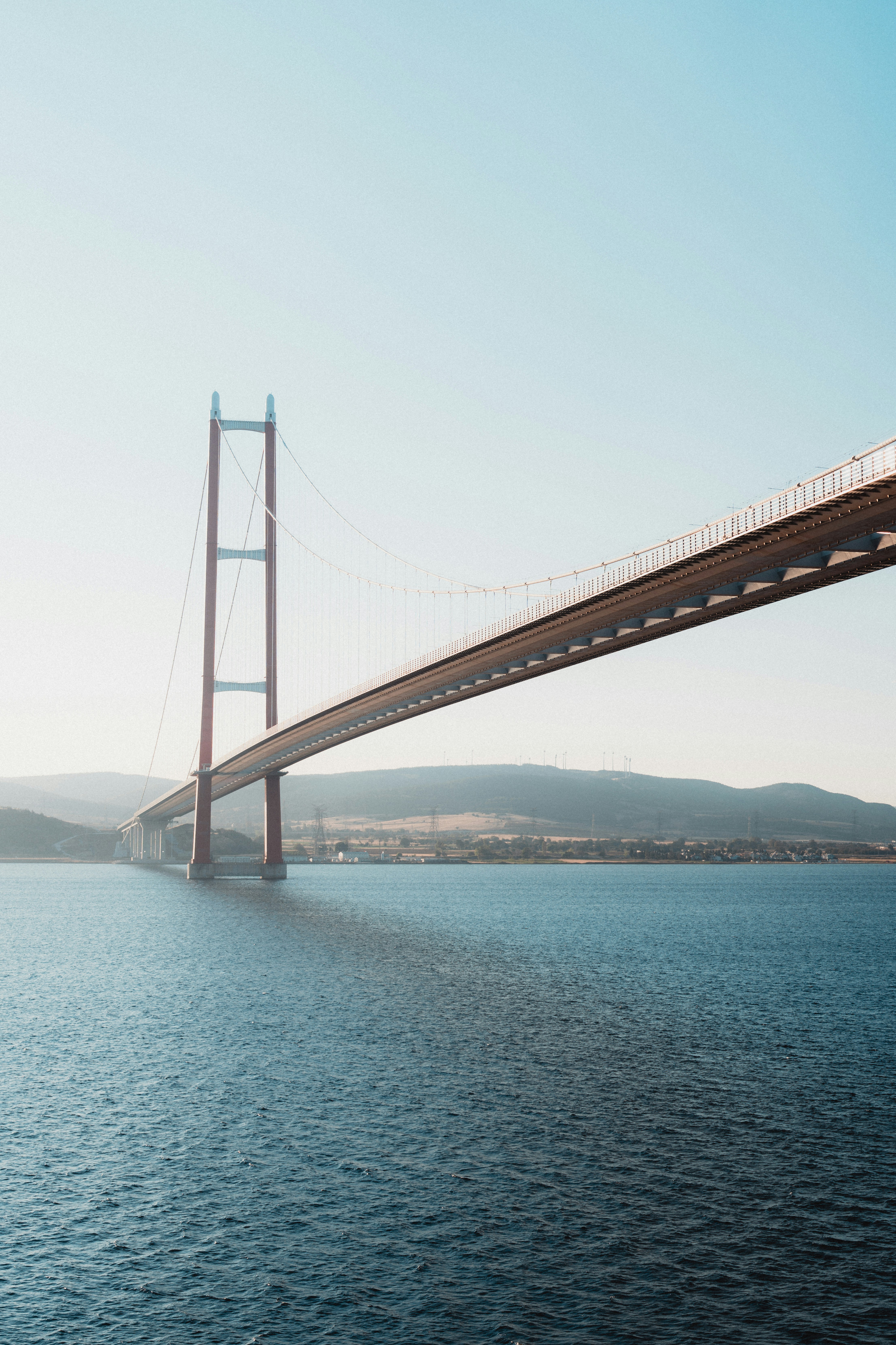 Suspension bridge over deep blue water with hills.