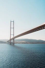 Suspension bridge over deep blue water with hills.