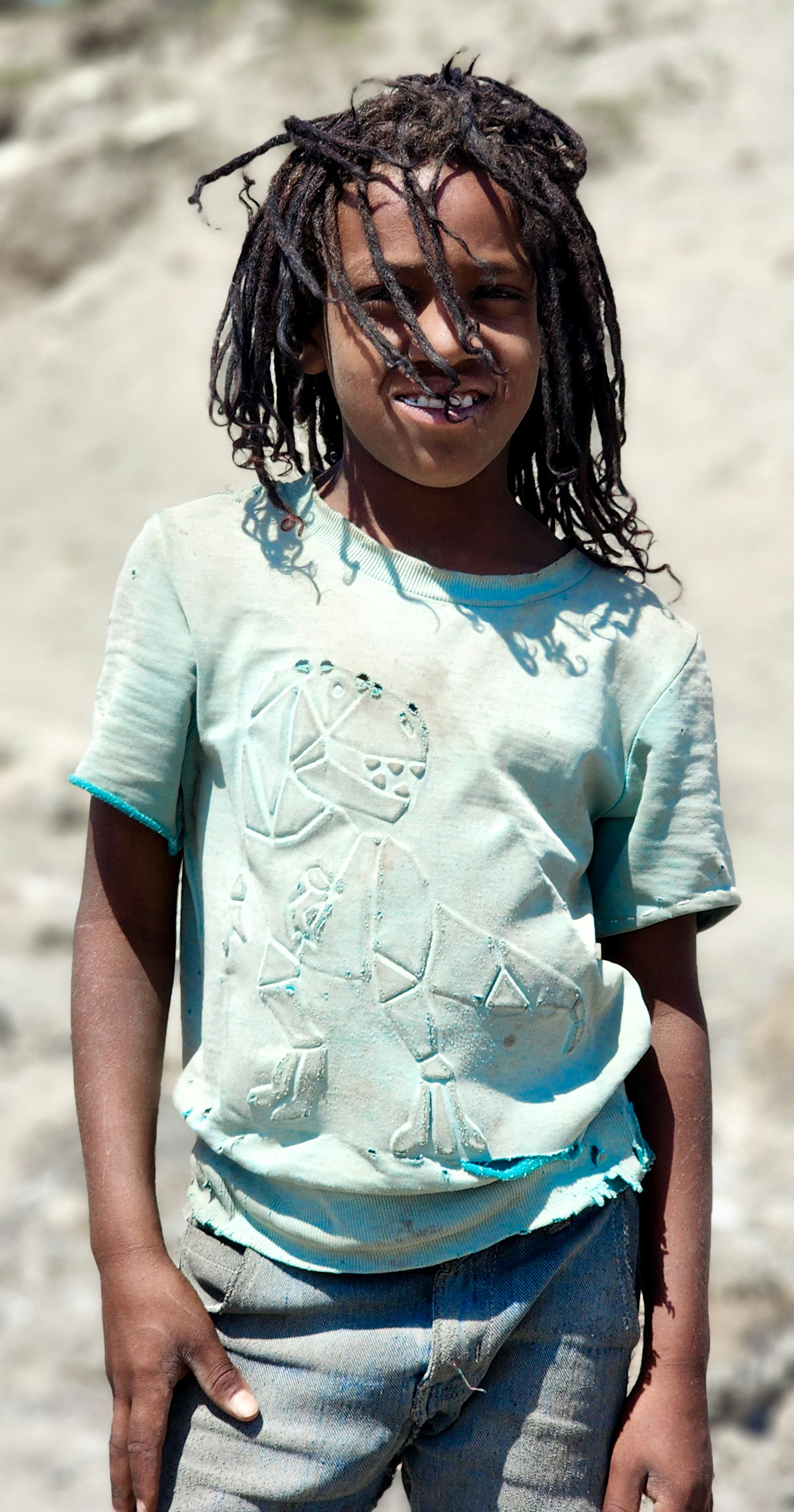 A young child with dreadlocks wearing a dinosaur t-shirt.