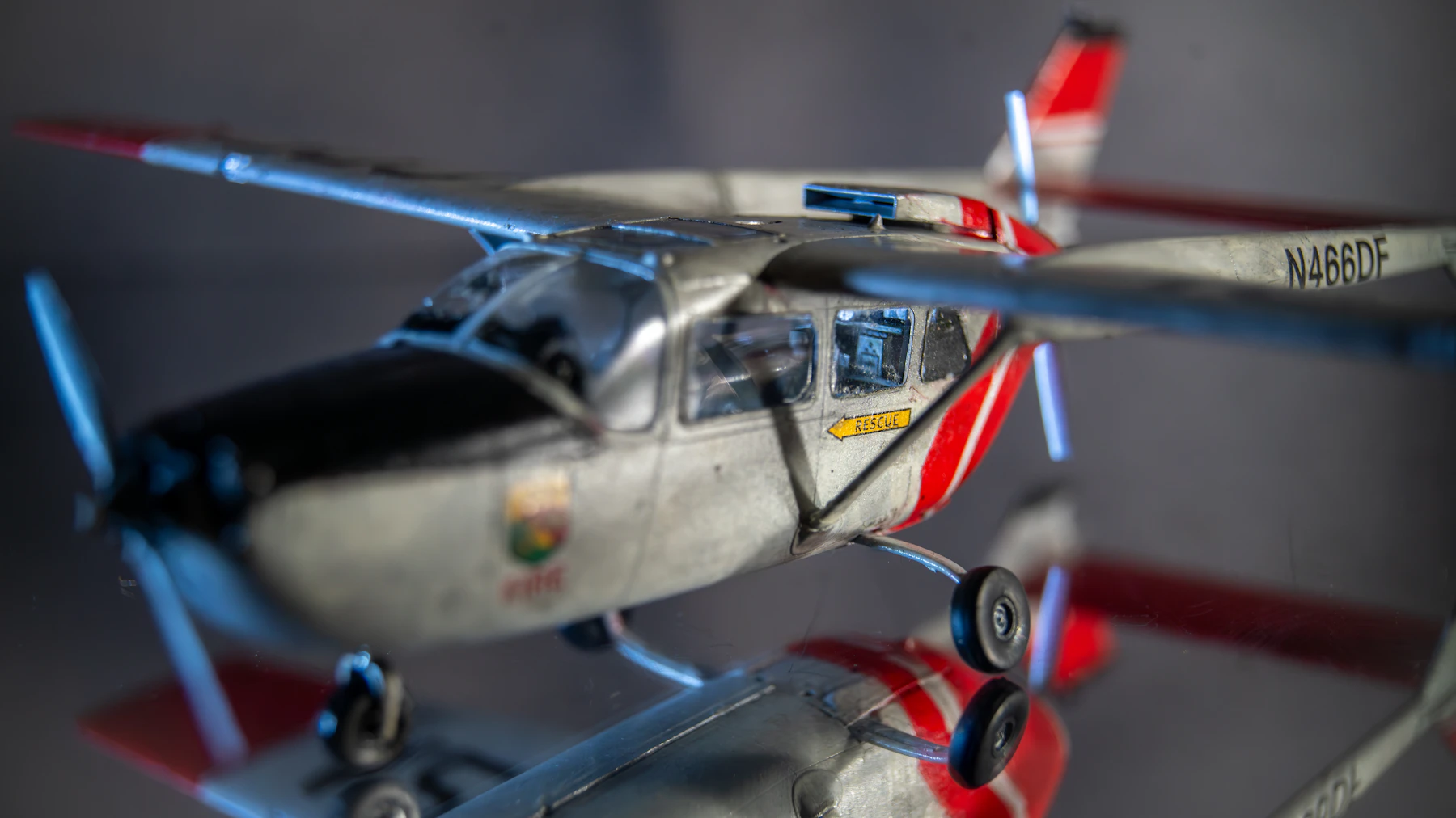 A finished silver-white light aircraft model with red stripes, standing on a mirror