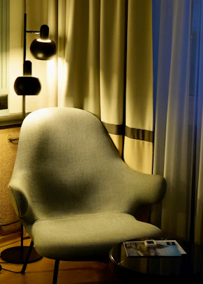A modern armchair next to a floor lamp and curtains