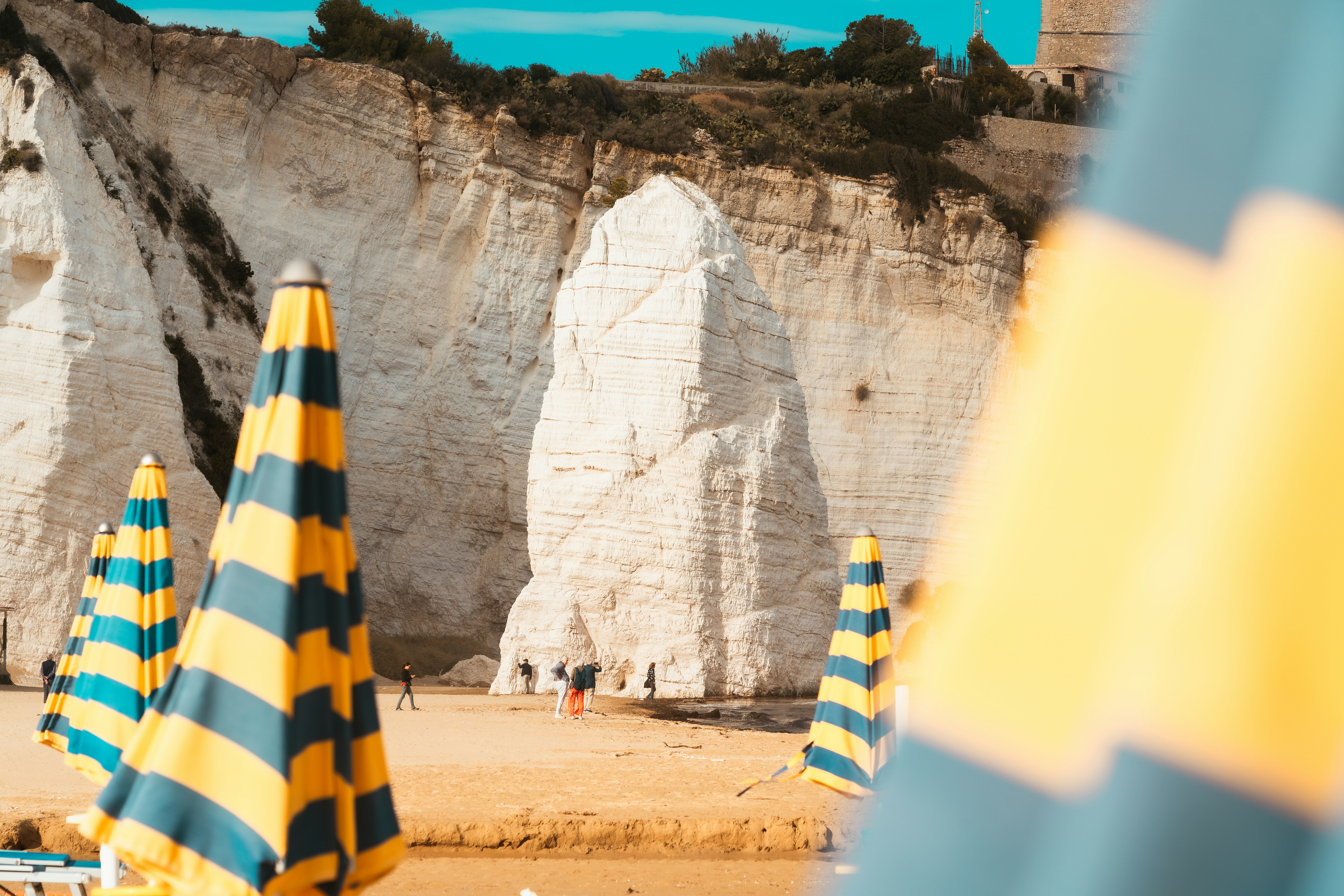 Beach umbrellas in front of white rocky cliffs.
