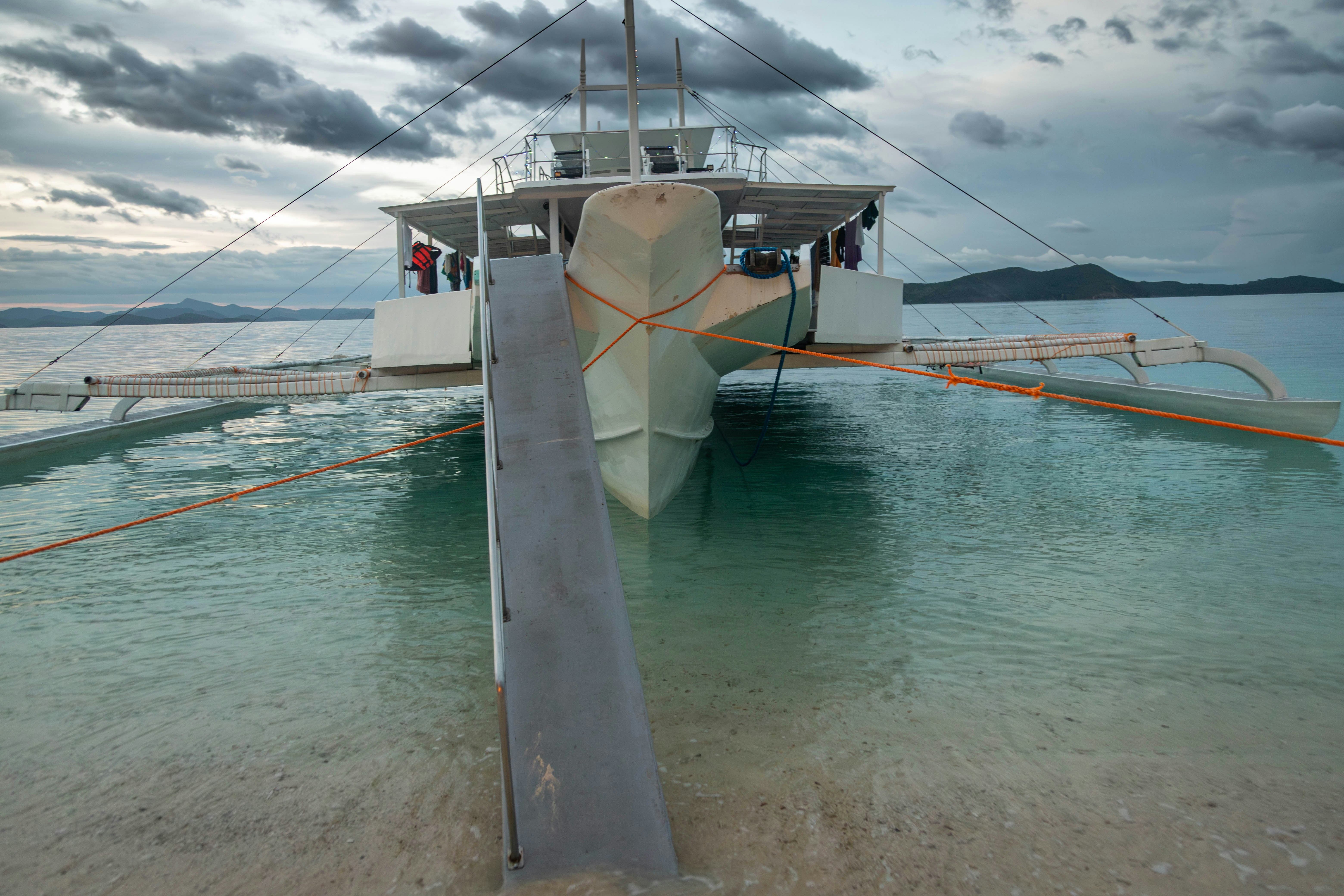 A catamaran boat docked near a sandy shore.