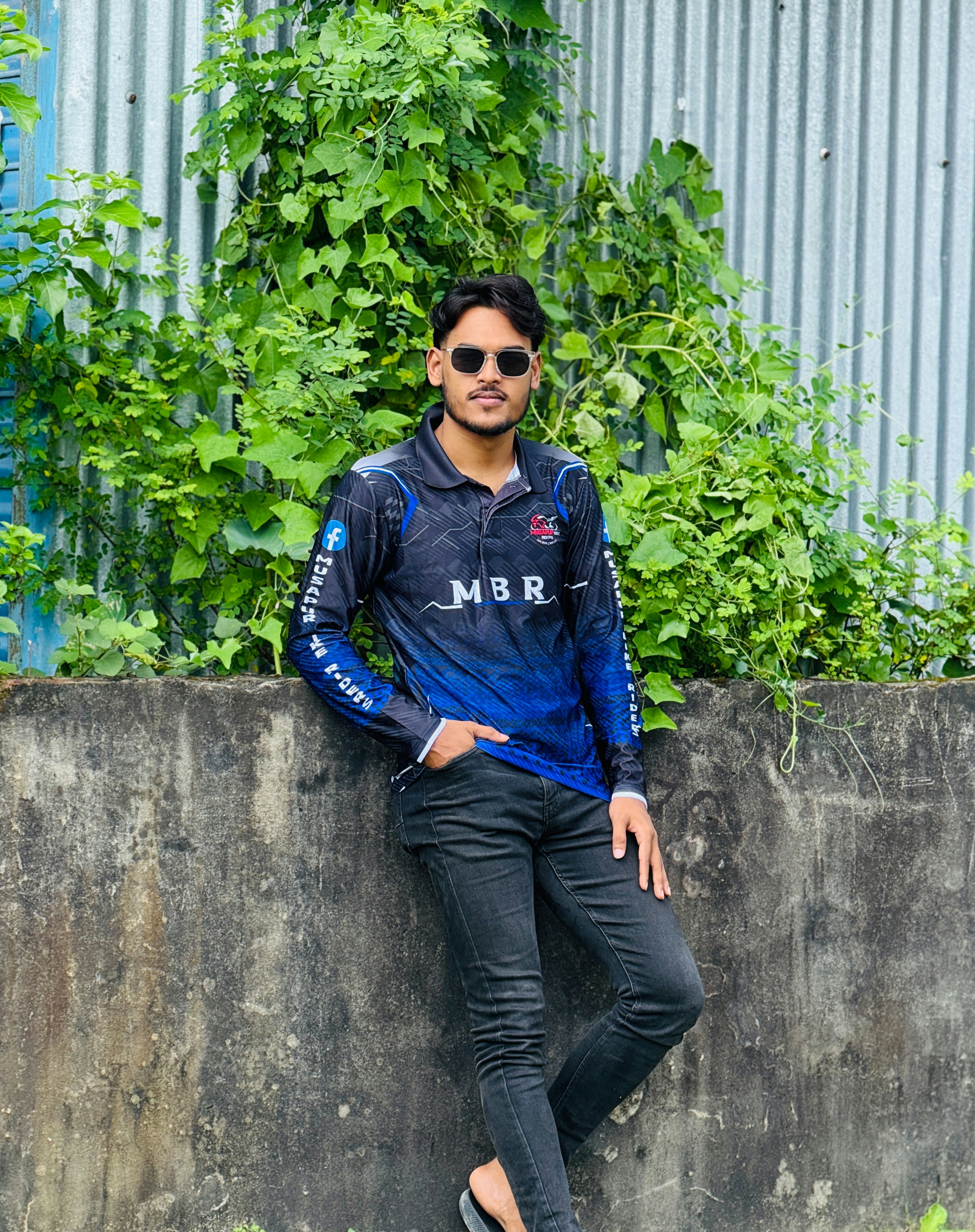 Man in sunglasses and blue shirt leans against wall