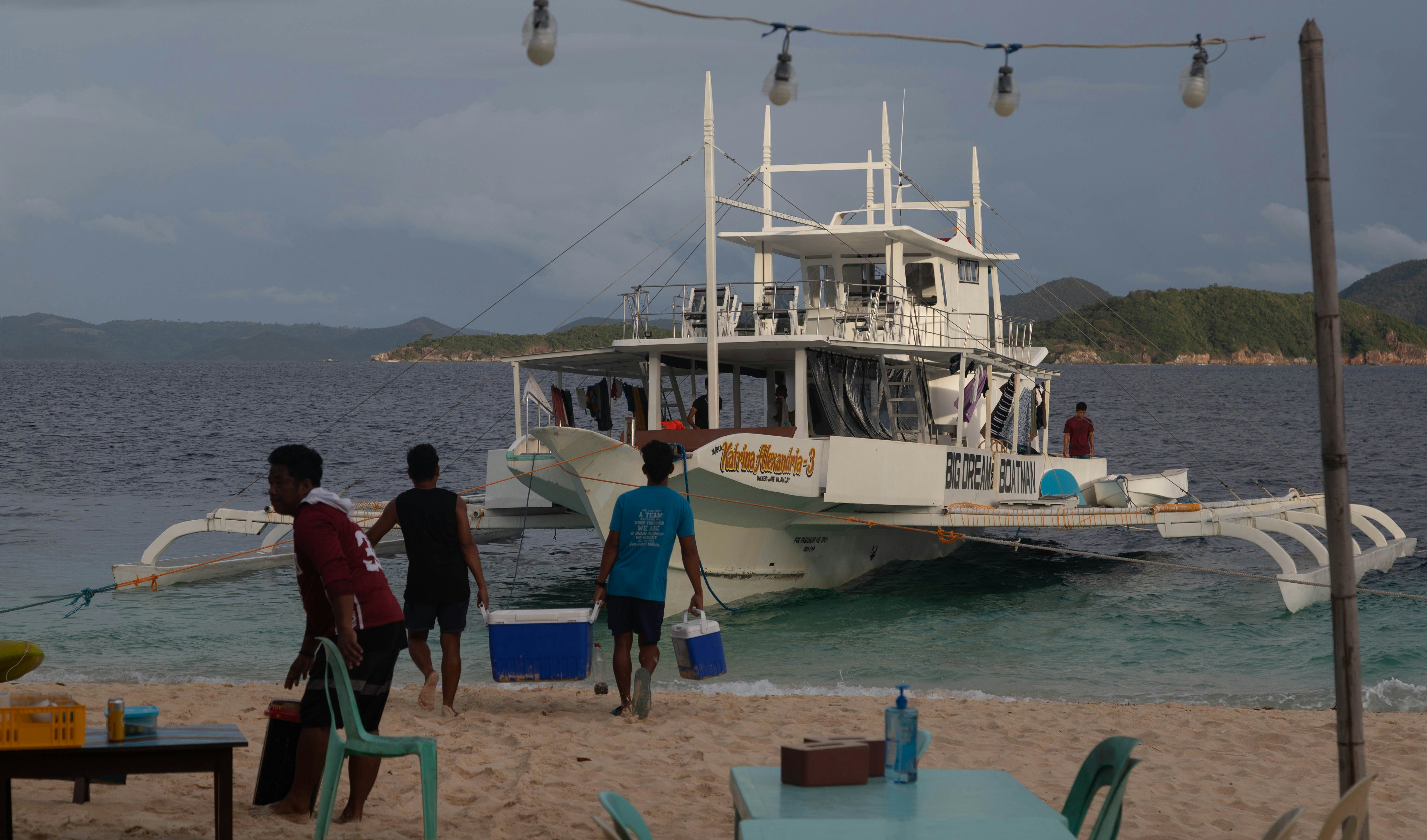 People disembarking a large boat on a sandy beach.