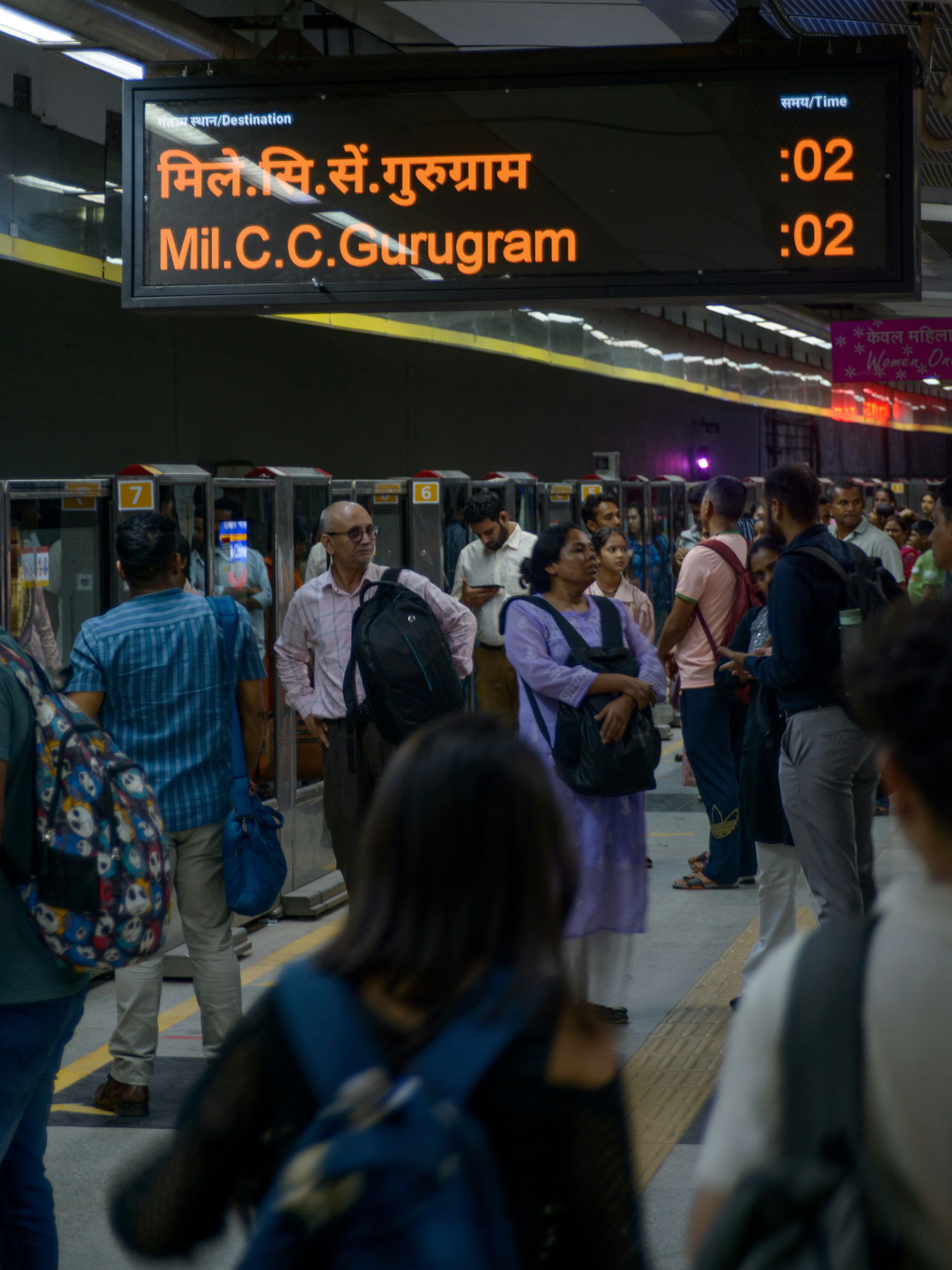 People waiting at a train station with digital display.