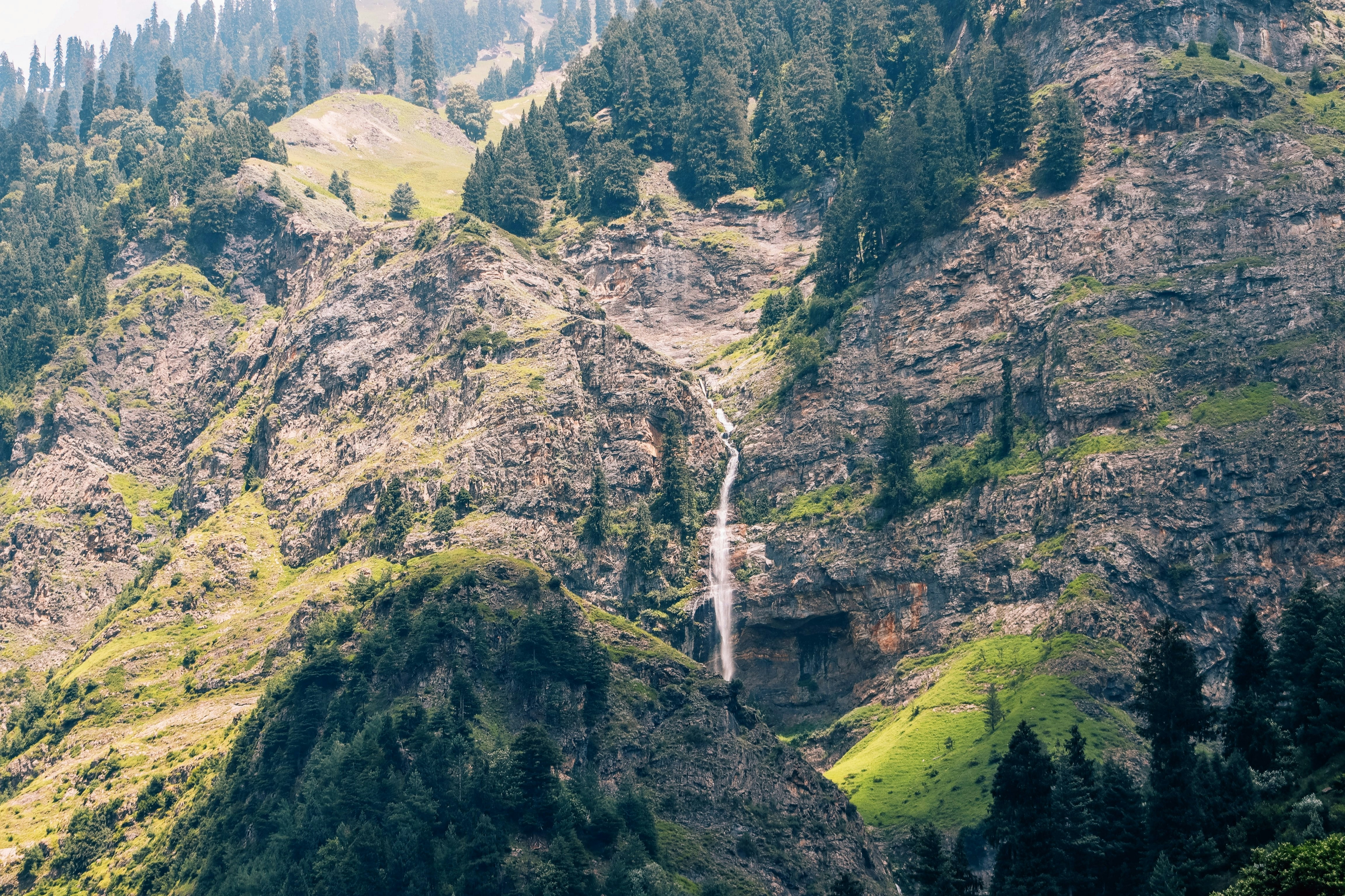 Chute d’eau en cascade sur un flanc de montagne rocheux et boisé.