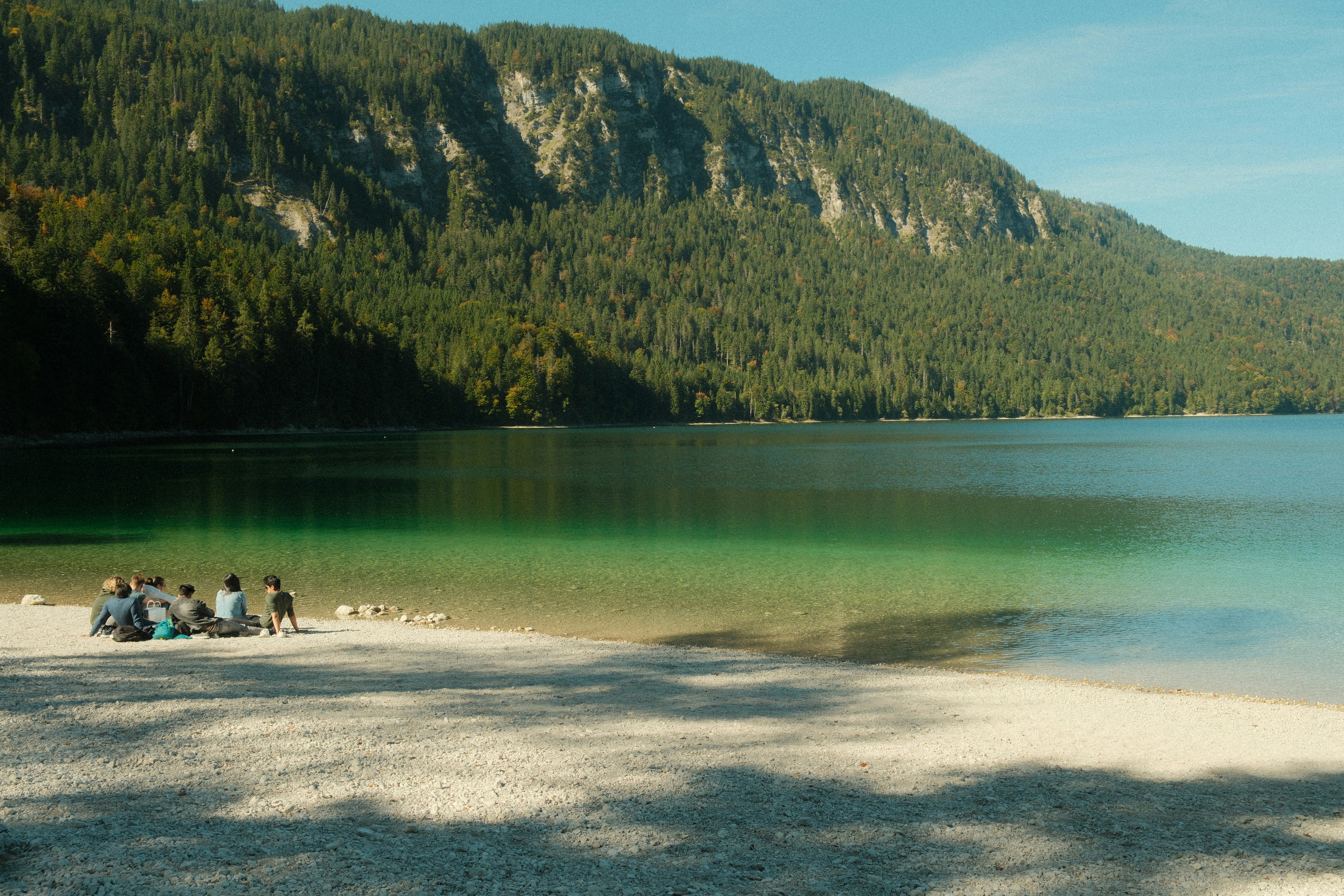 People relaxing on a beach by a clear lake
