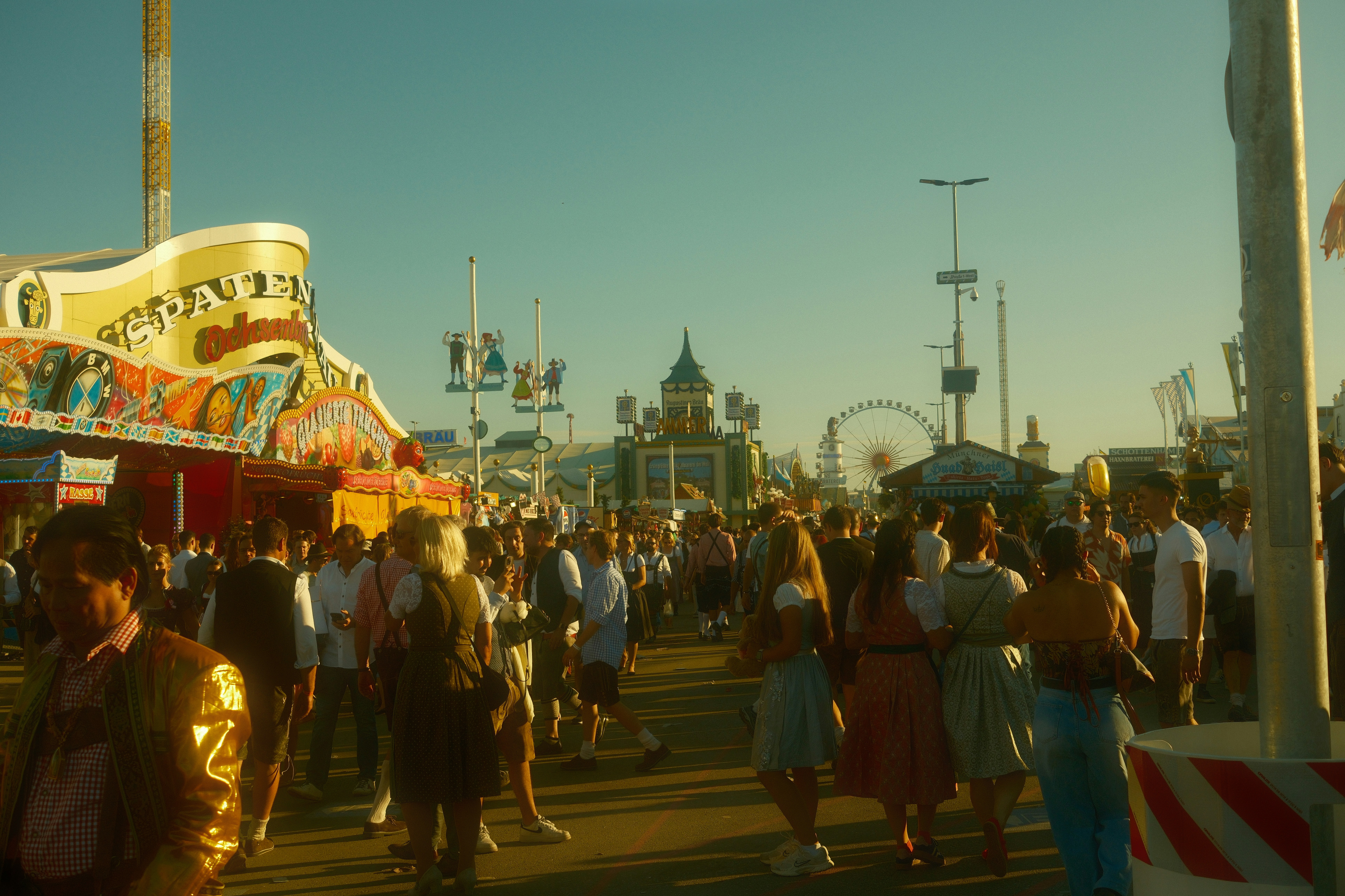 Crowd at a sunny outdoor amusement park with rides.