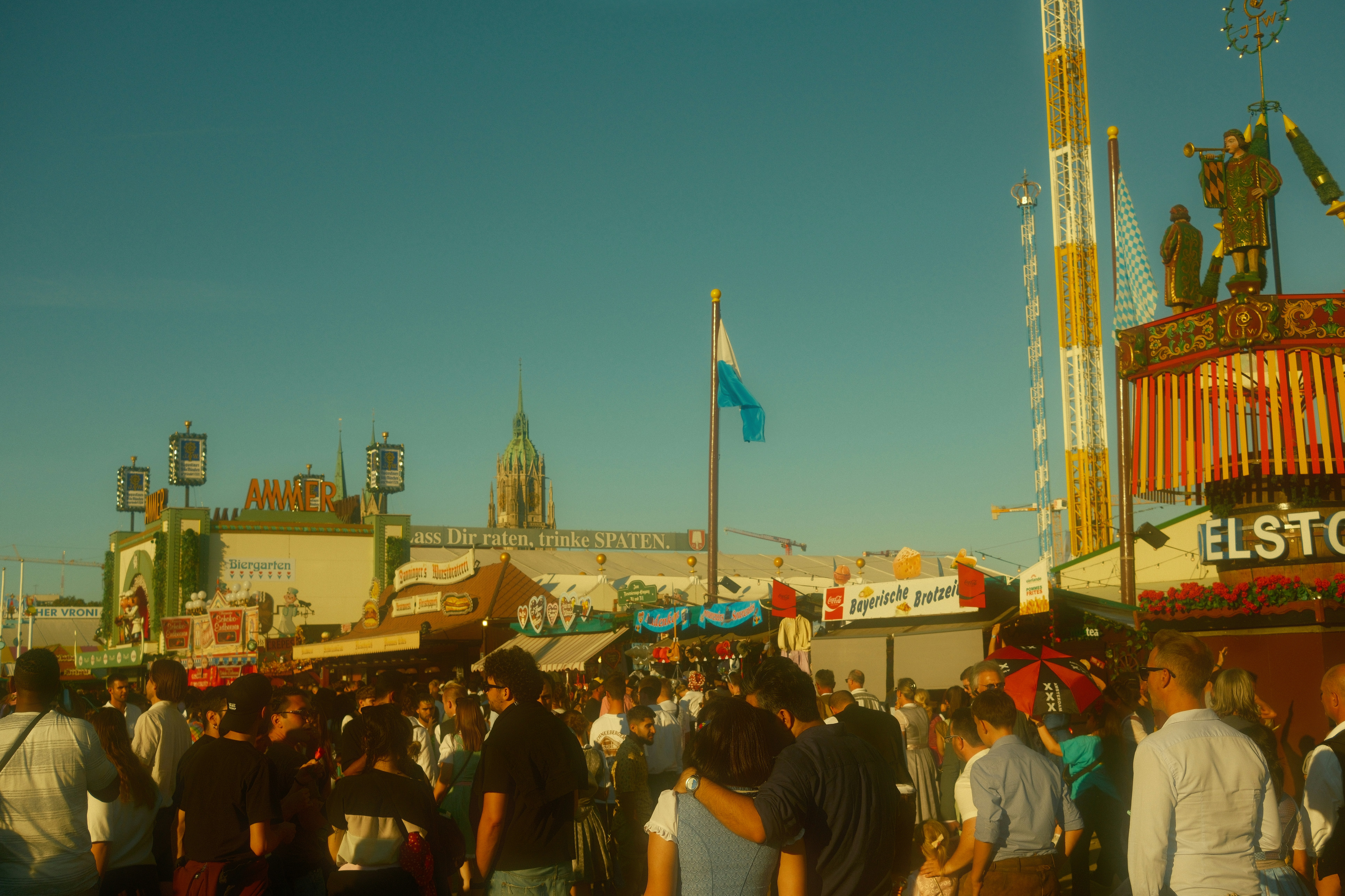 Crowded fairgrounds with rides and tents under blue sky