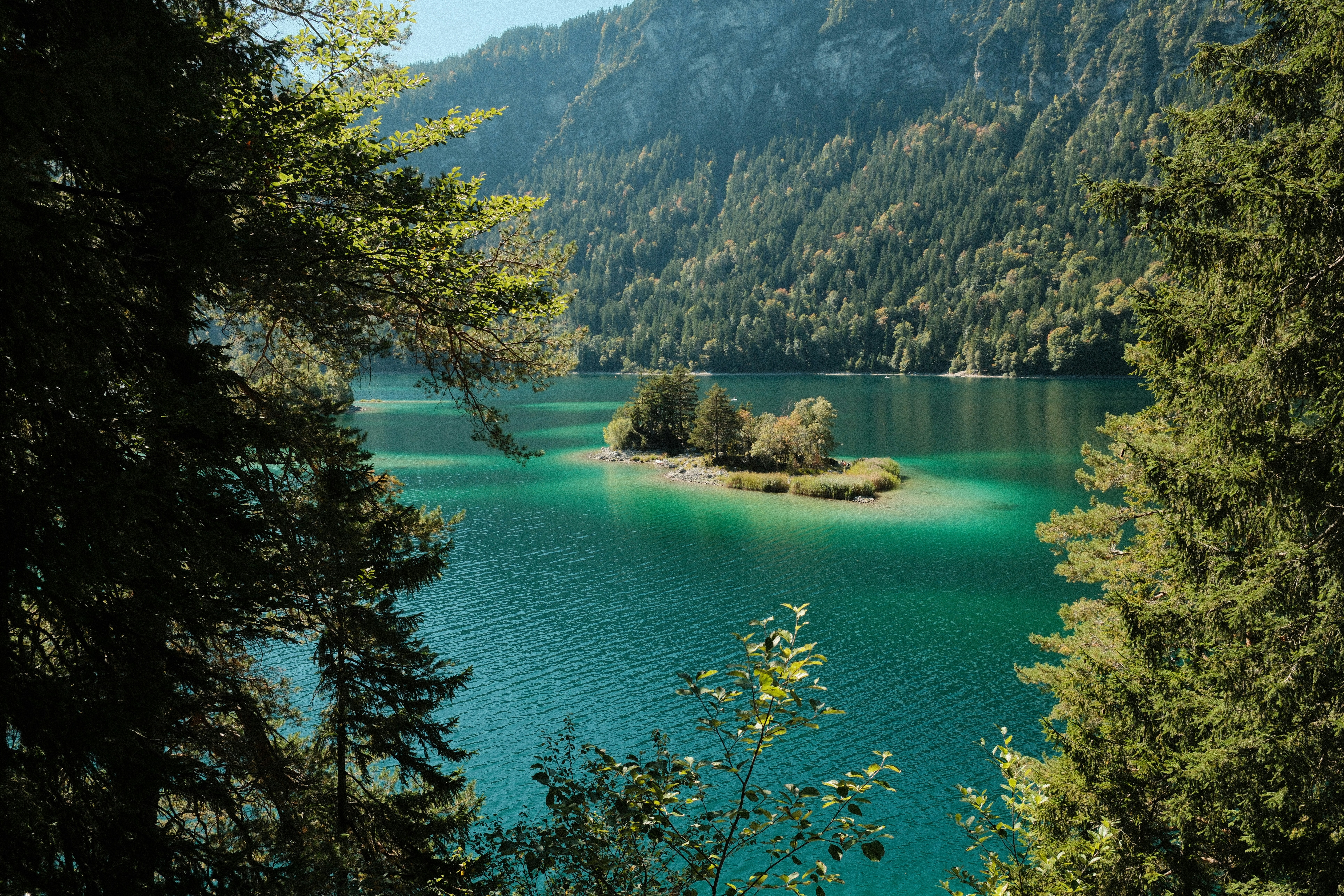 Turquoise lake with a small island and forested mountains.