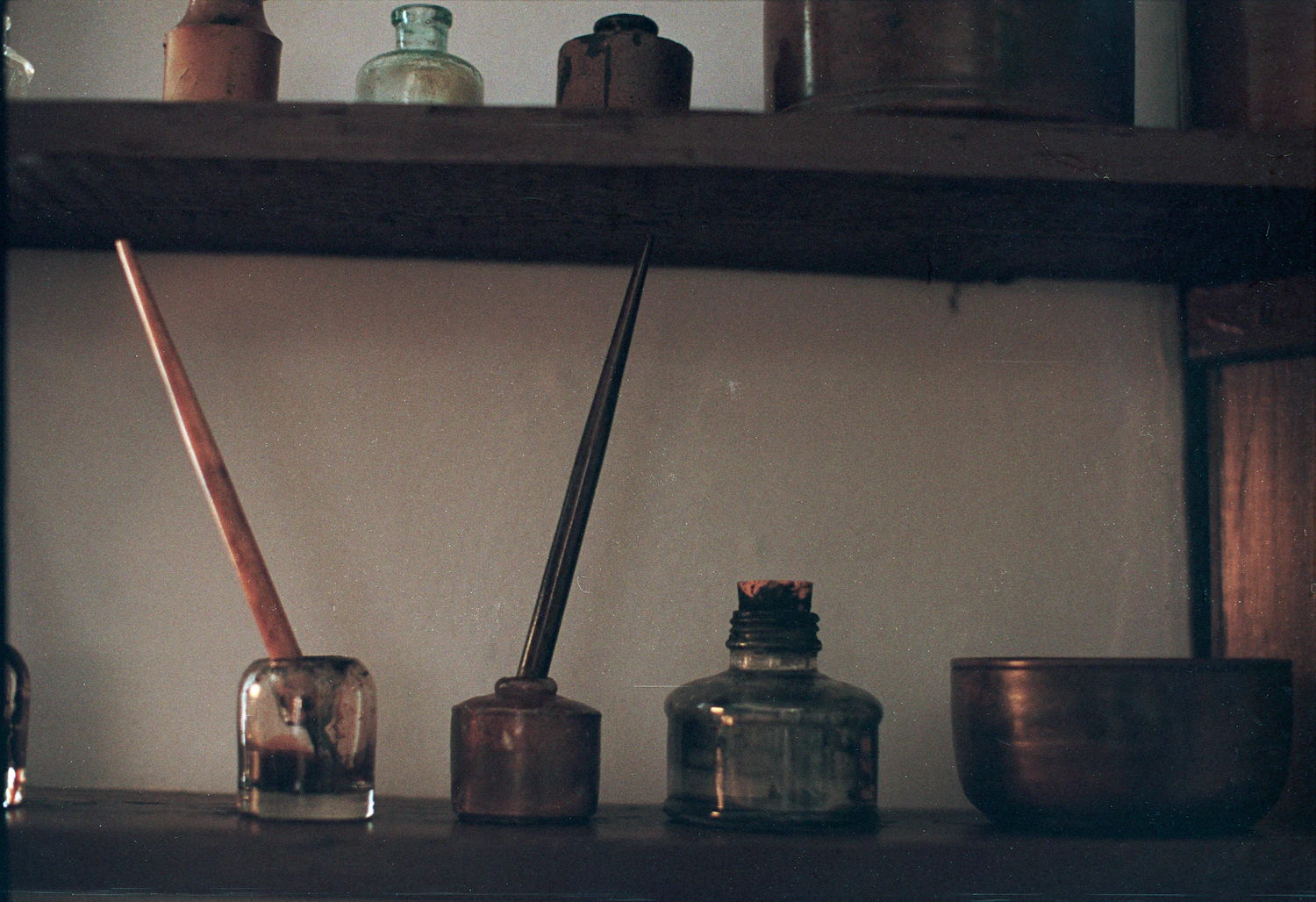 Dip pens standing in open ink bottles on a dark shelf