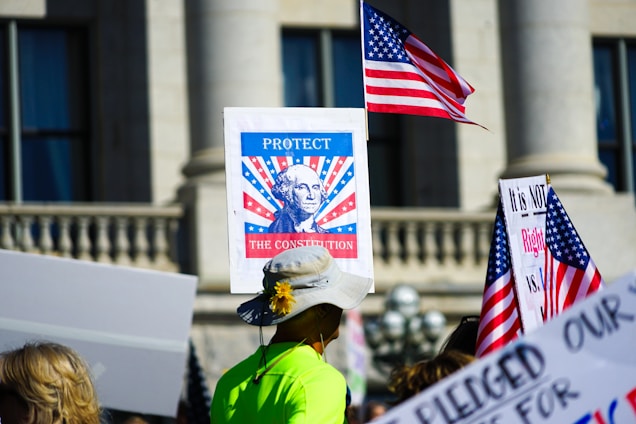 Protestors hold signs and american flags outside building.