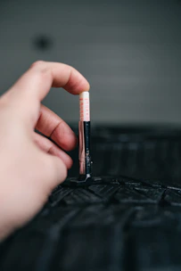 Hand measuring tire tread depth with gauge.