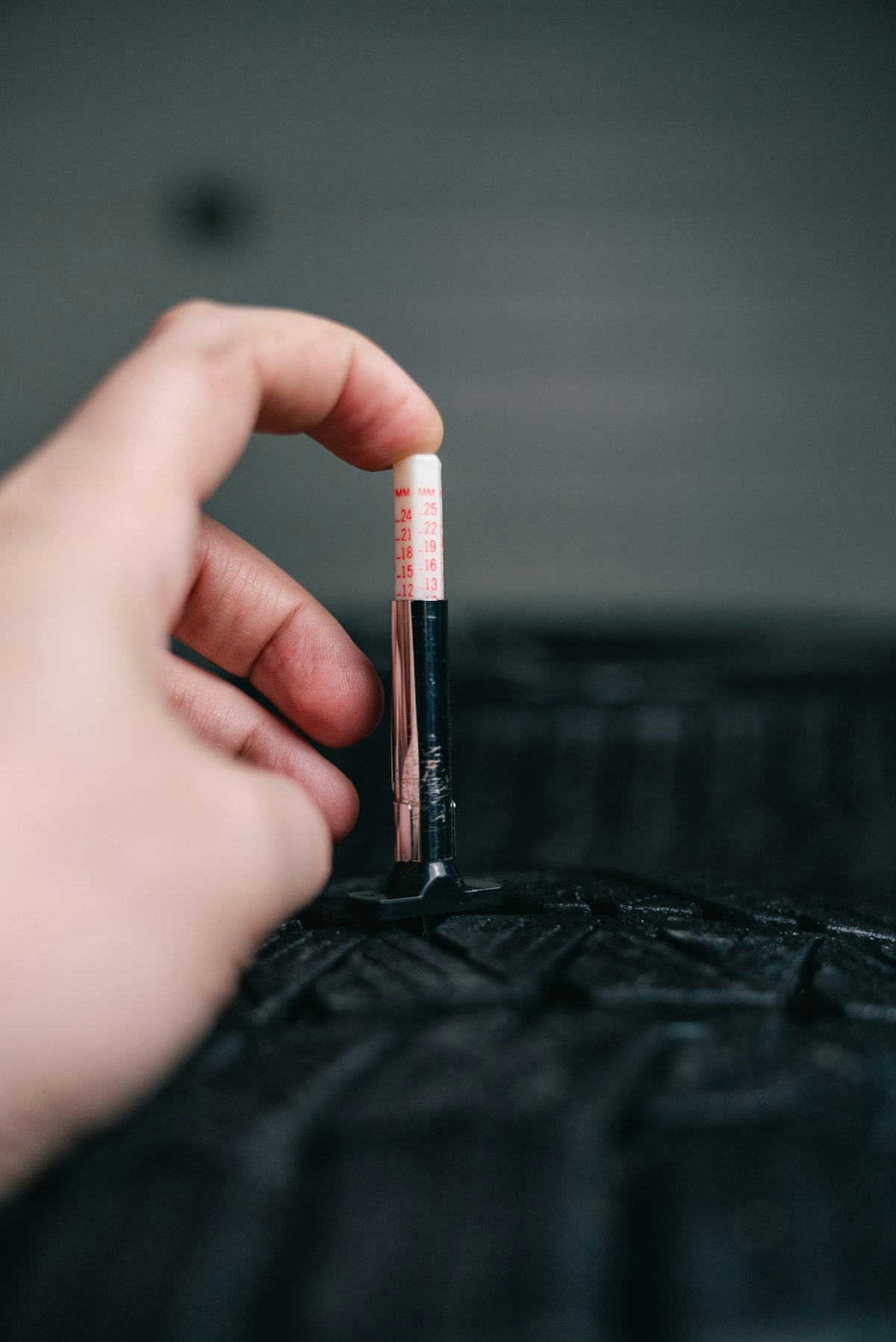 Hånd som måler mønsterdybde på bildekk med dekkdybdemåler