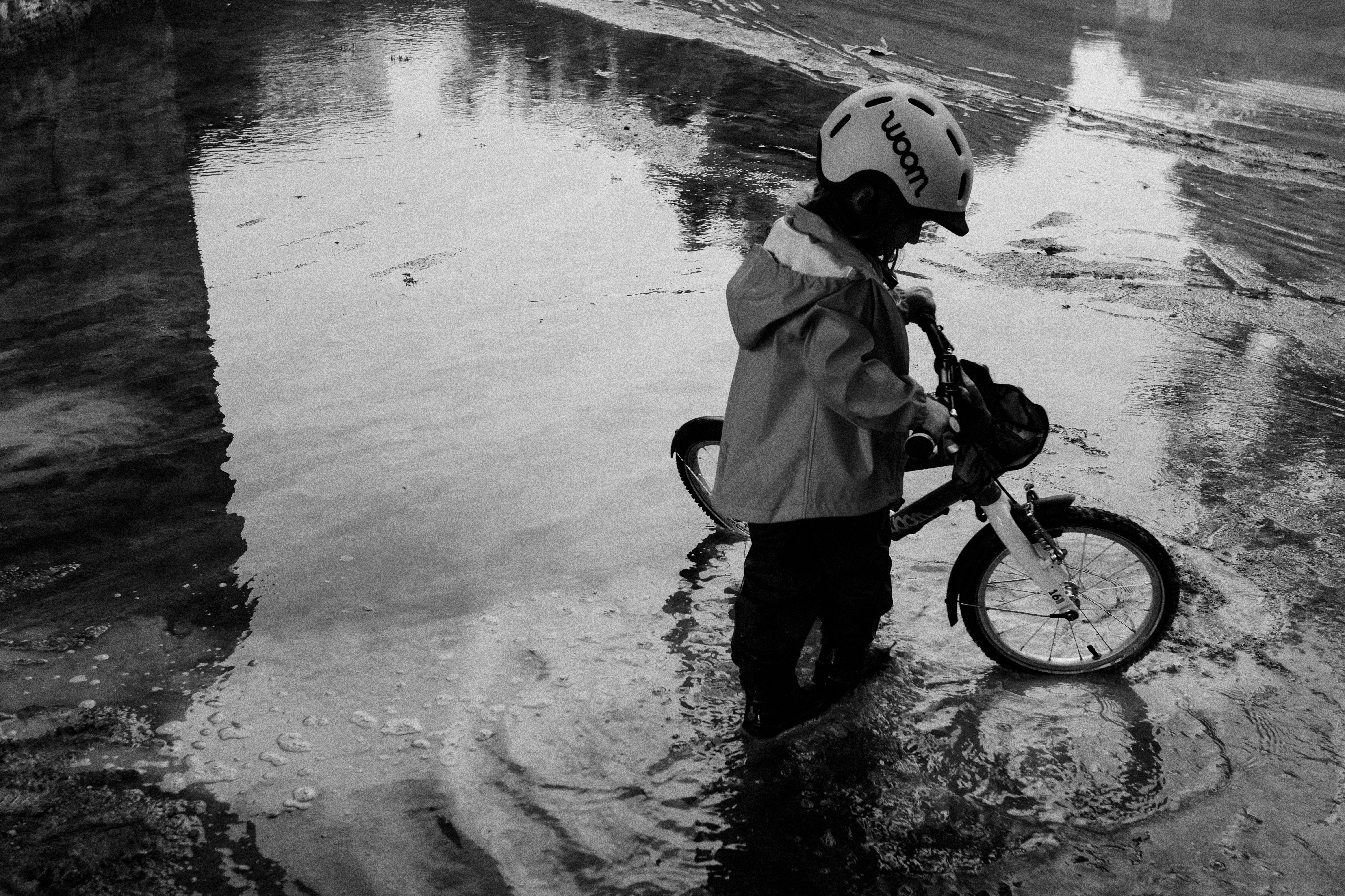 Child in helmet stands with bicycle in puddle