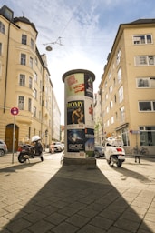 Circular advertising column on a sunny city street.