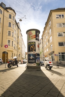 Circular advertising column on a sunny city street.