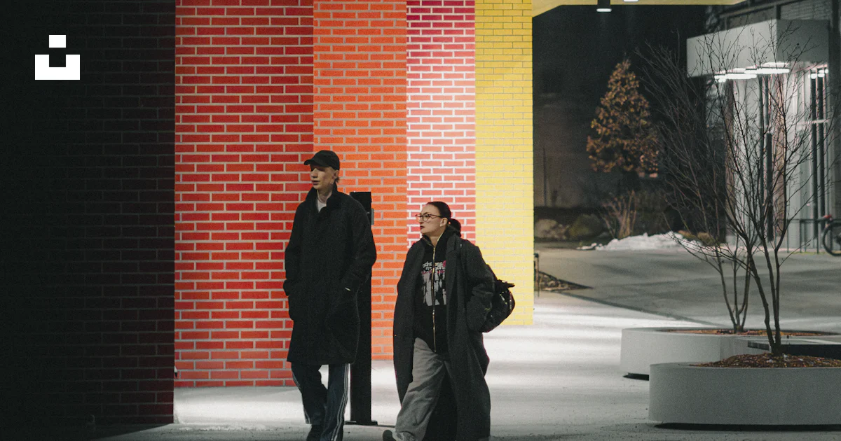 Two people walk past colorful modern building at night. photo – Free ...