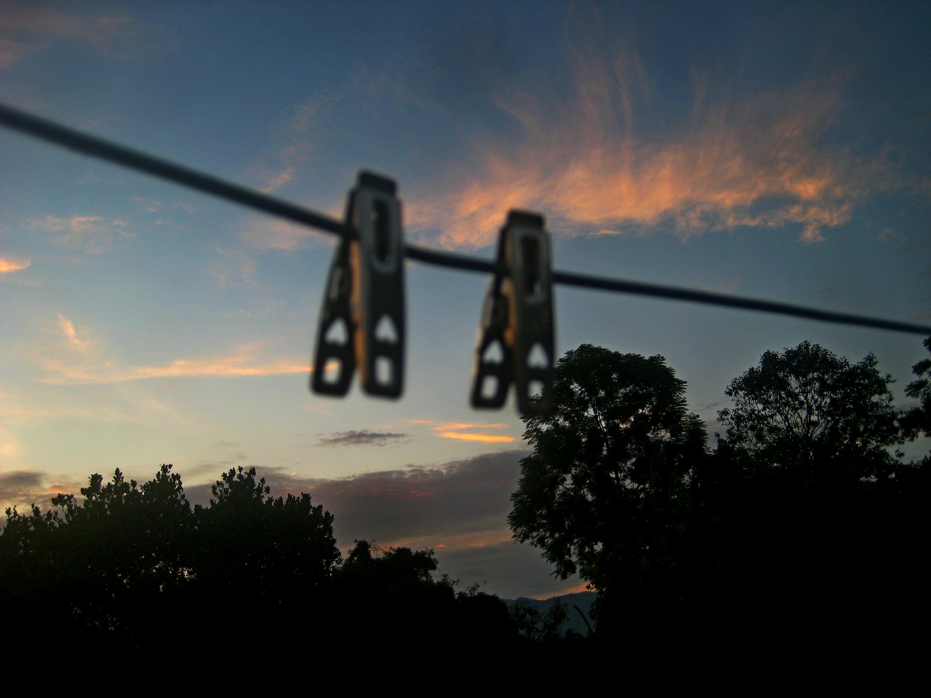 Two clothespins hang on a wire at sunset.