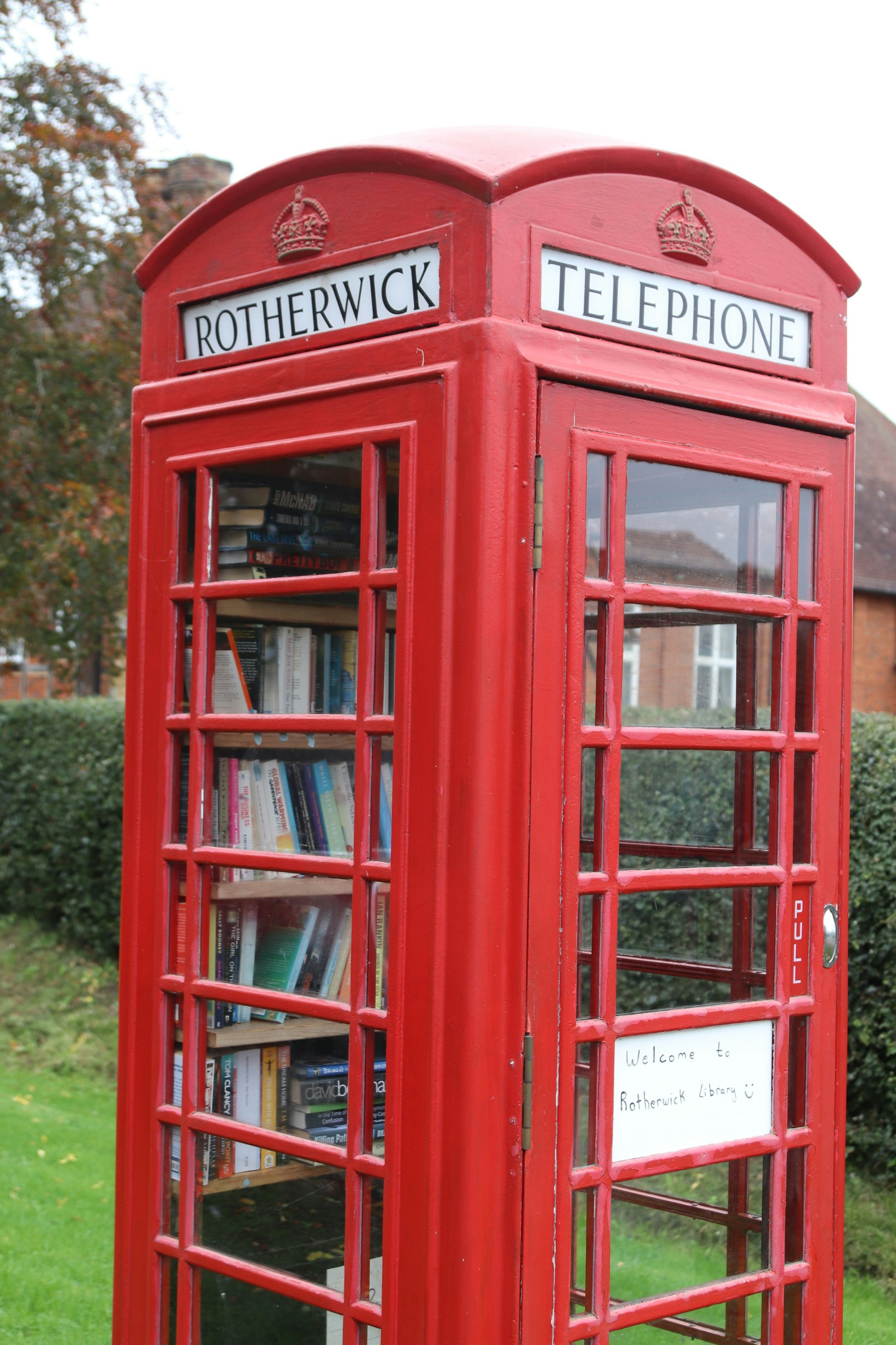 Red telephone box filled with books in a garden.