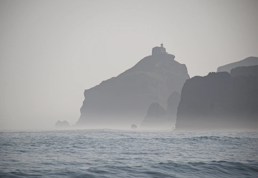 Misty sea cliffs with a lighthouse in the distance