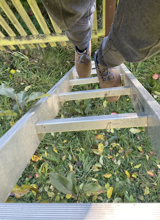 Person climbing a ladder in a grassy yard.