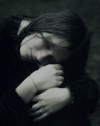 A young woman with dark hair embraces herself.