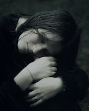 A young woman with dark hair embraces herself.
