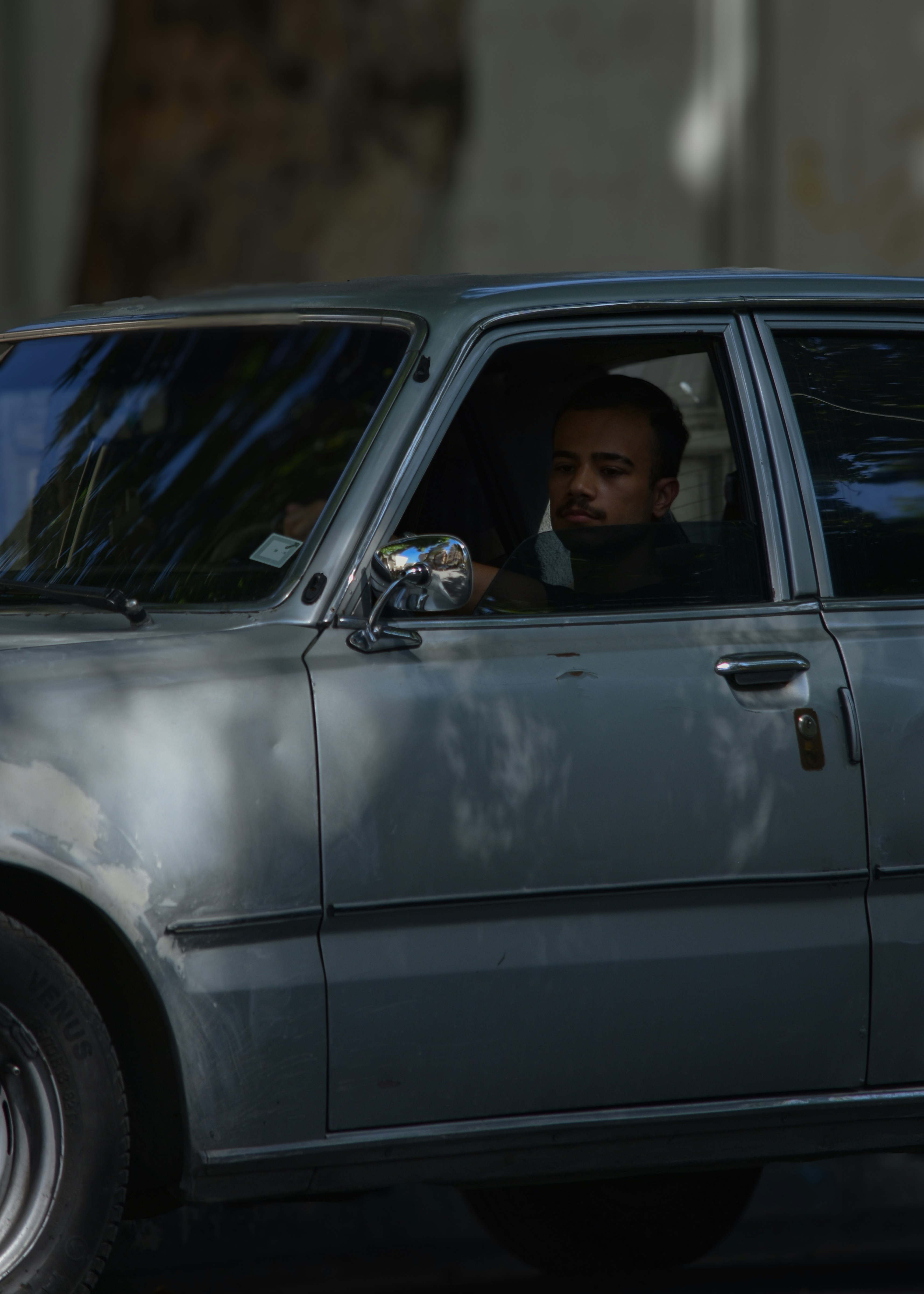 Homem dirigindo um carro velho de prata