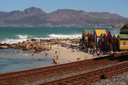 Colorful beach huts on a sandy shore with mountains.