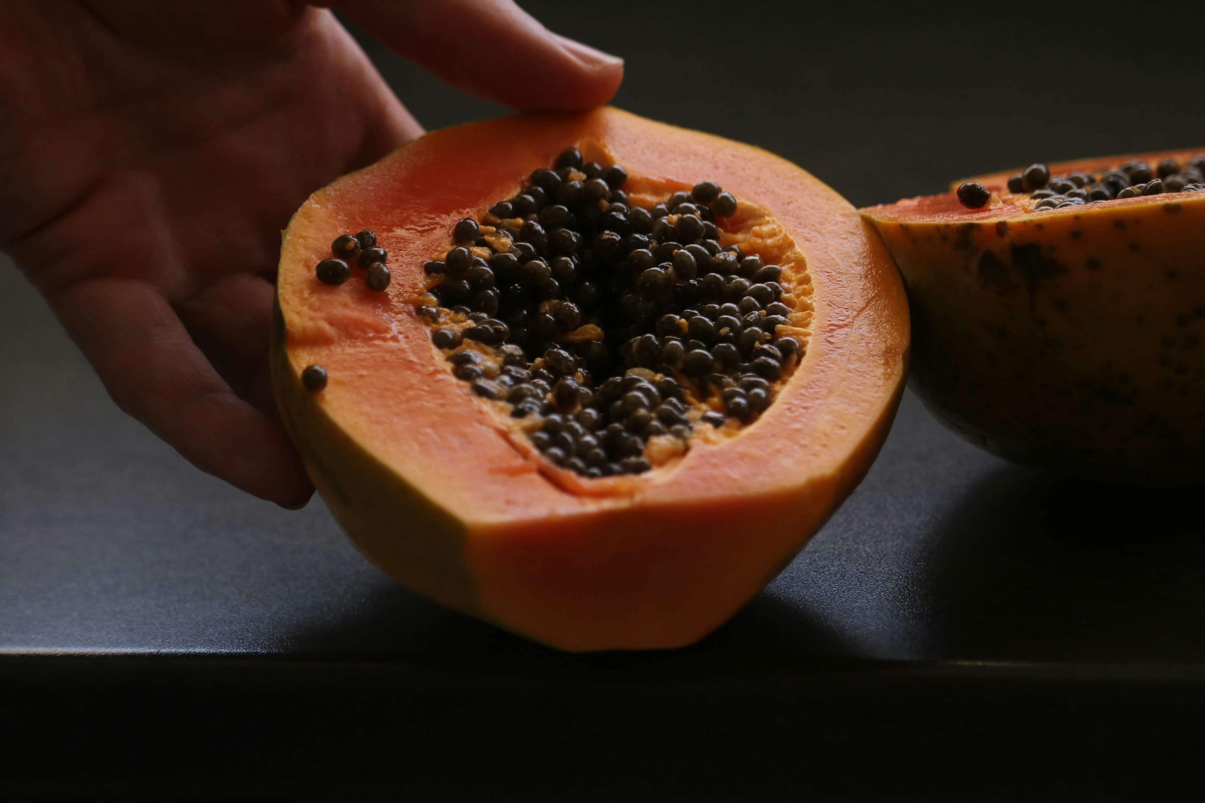 A hand holding a cut papaya with black seeds.