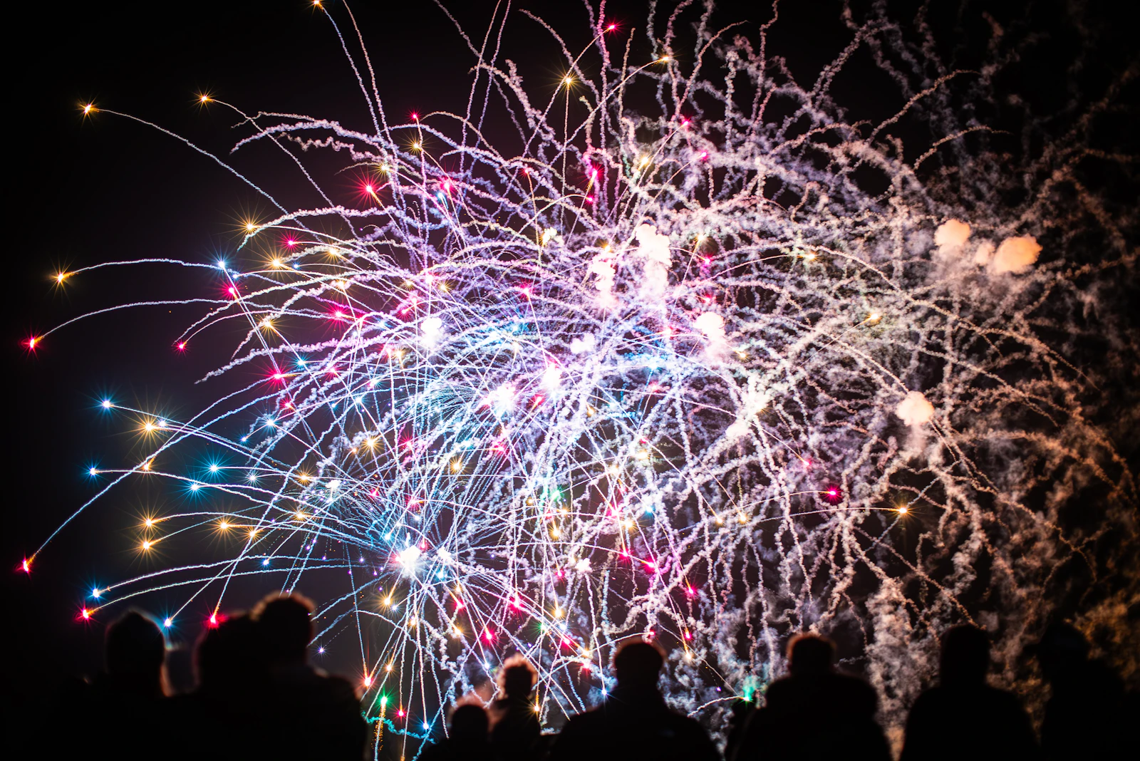 Colourful fireworks bursting over a crowd silhouetted against the night sky